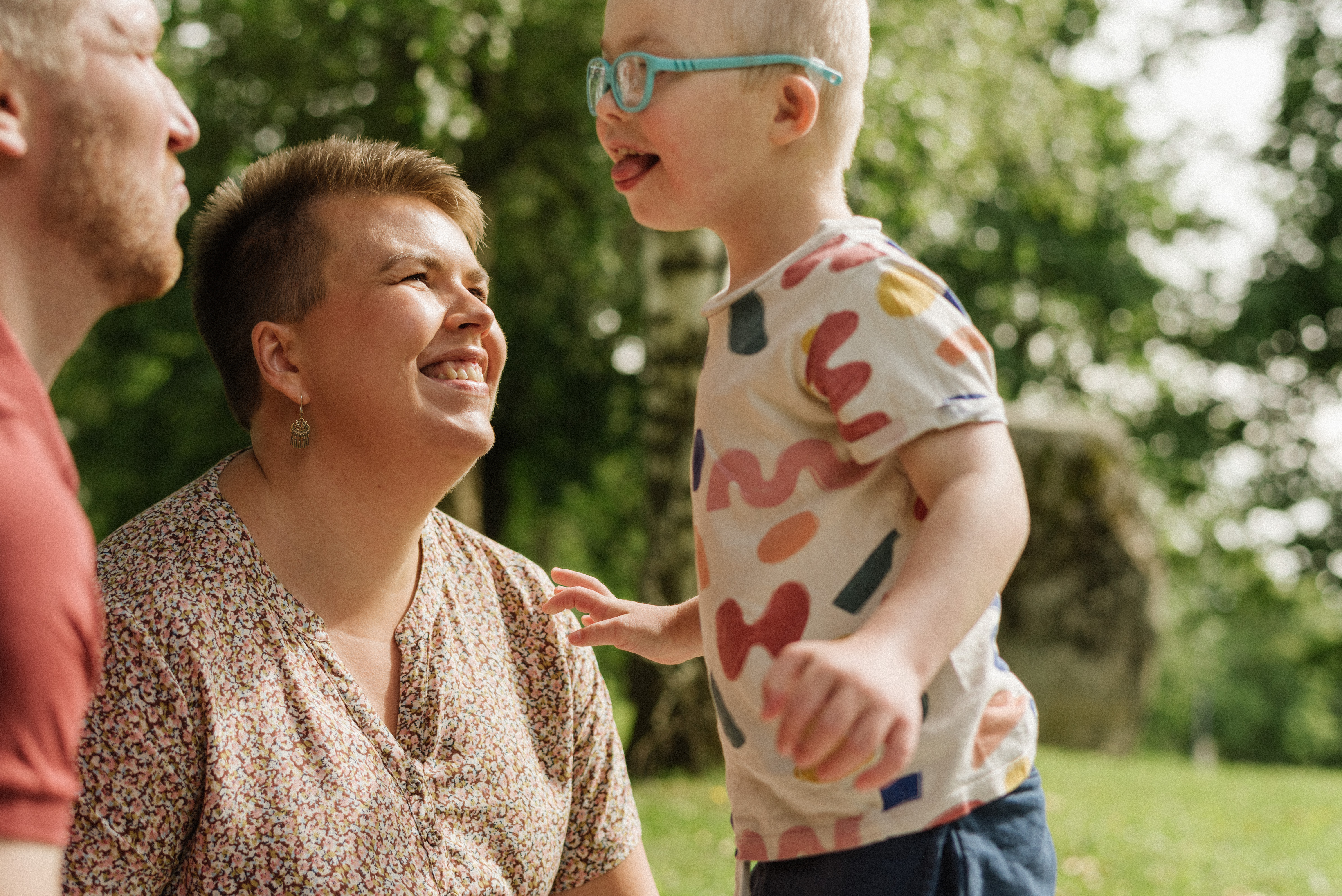 Äiti katsoo hymyillen pientä poikaansa, joka näyttää kieltä vanhemmilleen. En mamma tittar leende på sin lille son som räcker ut tungan åt sina föräldrar.
