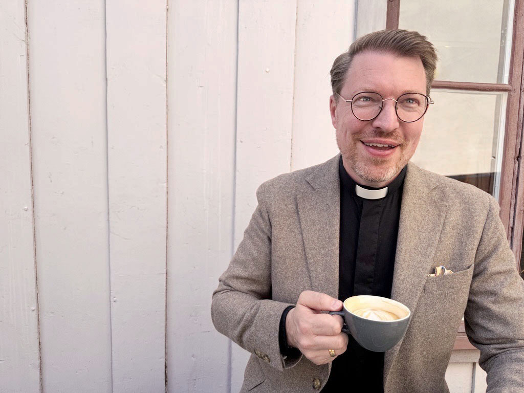 Dan Nässelqvist med en kaffekopp framför en vit trävägg