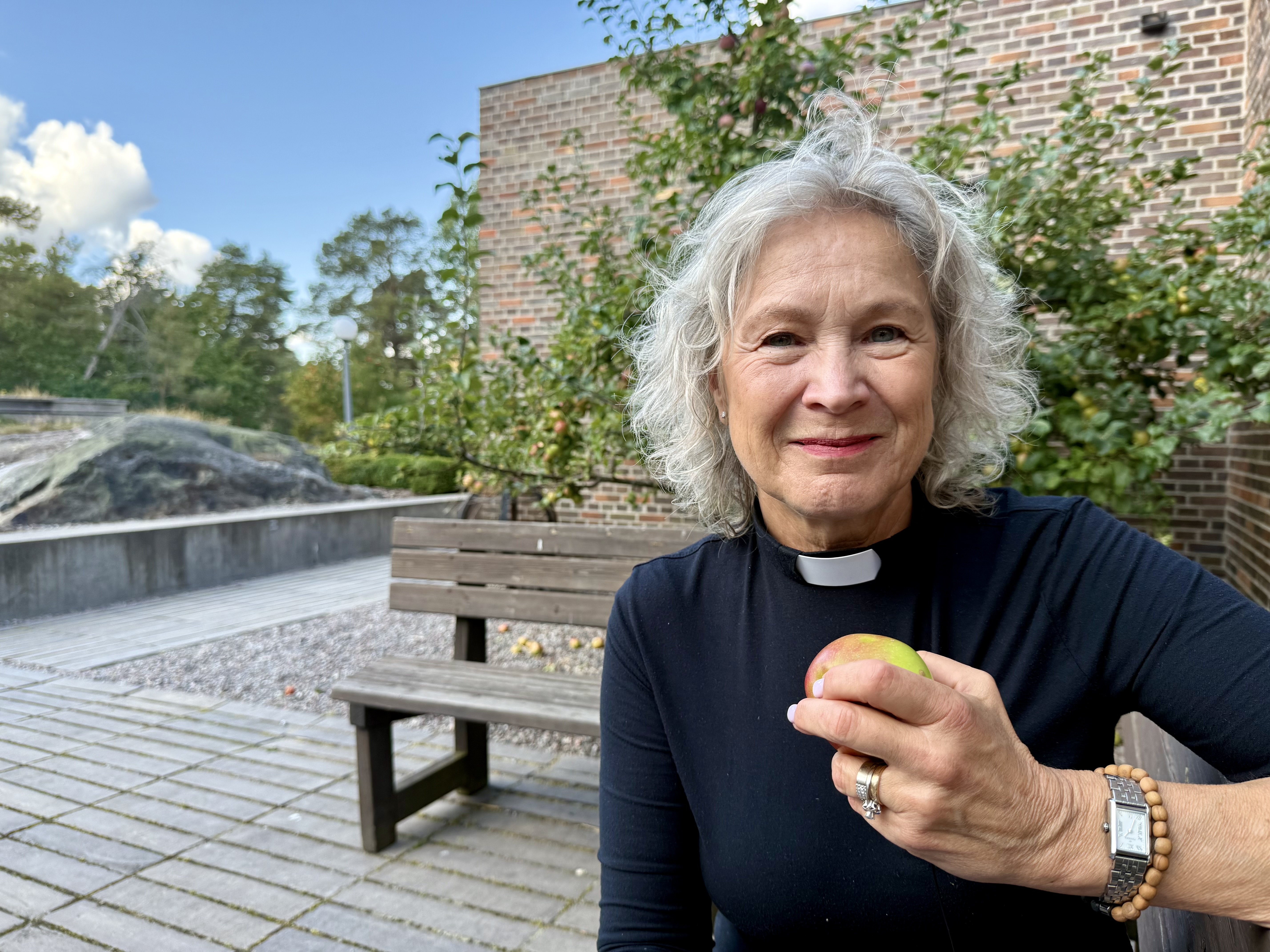 Kyrkoherde Marie Rehnstam framför ett äppelträd utanför Årsta kyrka