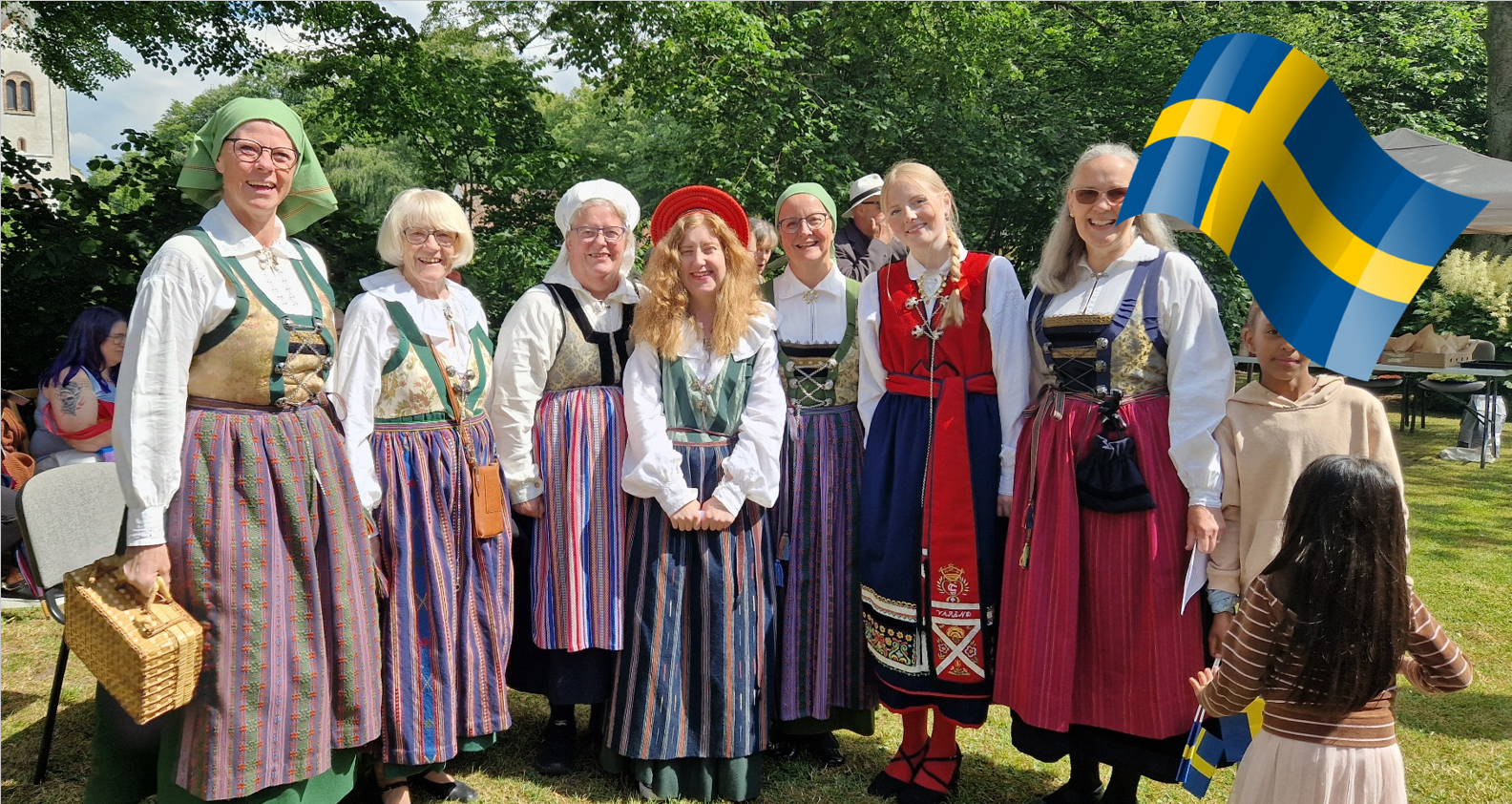 Sju glada kvinnor i folkdräkt och en svensk flagga.