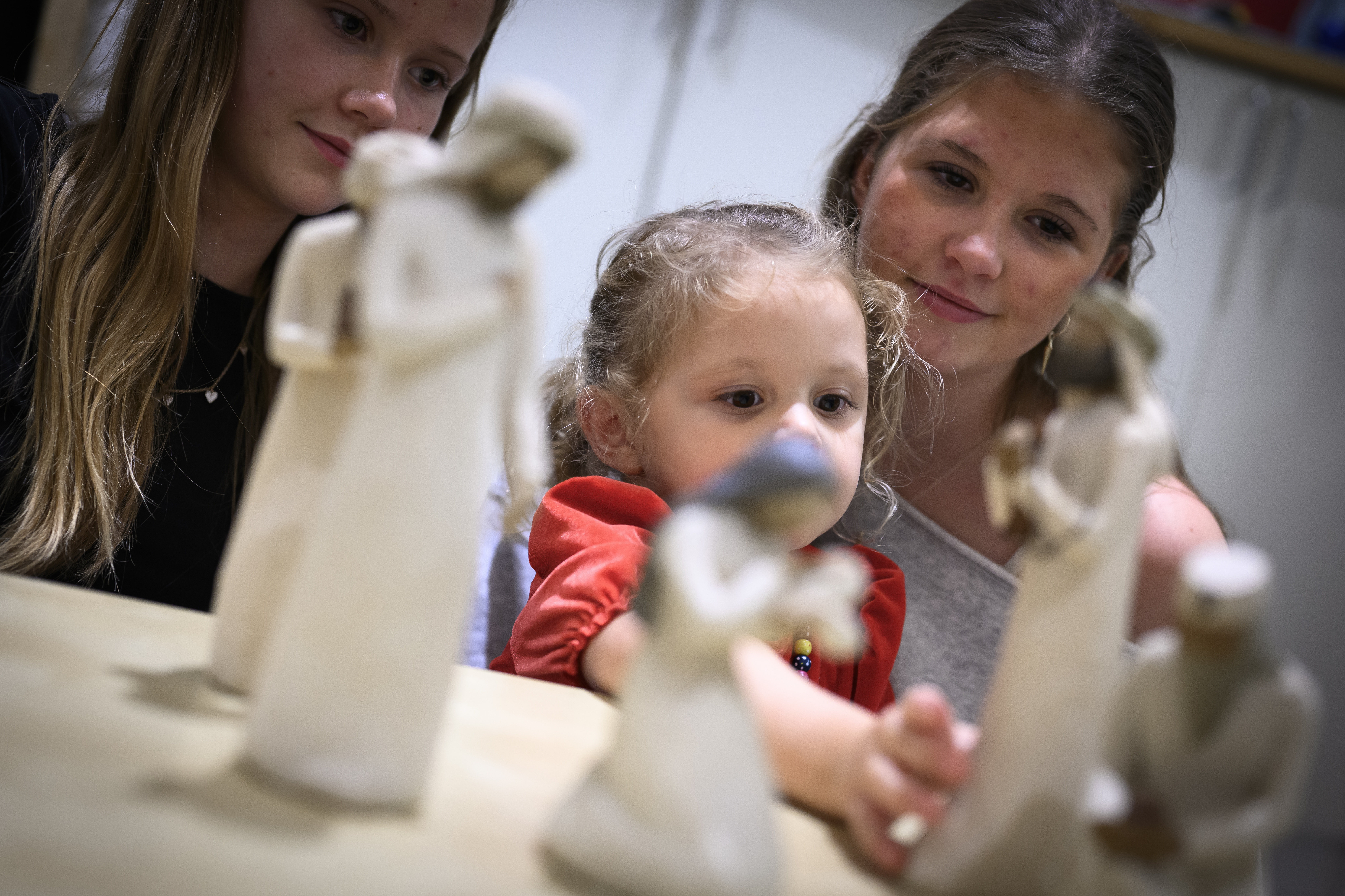 Trädockor som föreställer Jungfru Maria med Jesus-barnet i famnen och de tre vise männen står på ett bord. Ett barn och två ungdomar sitter runt bordet.