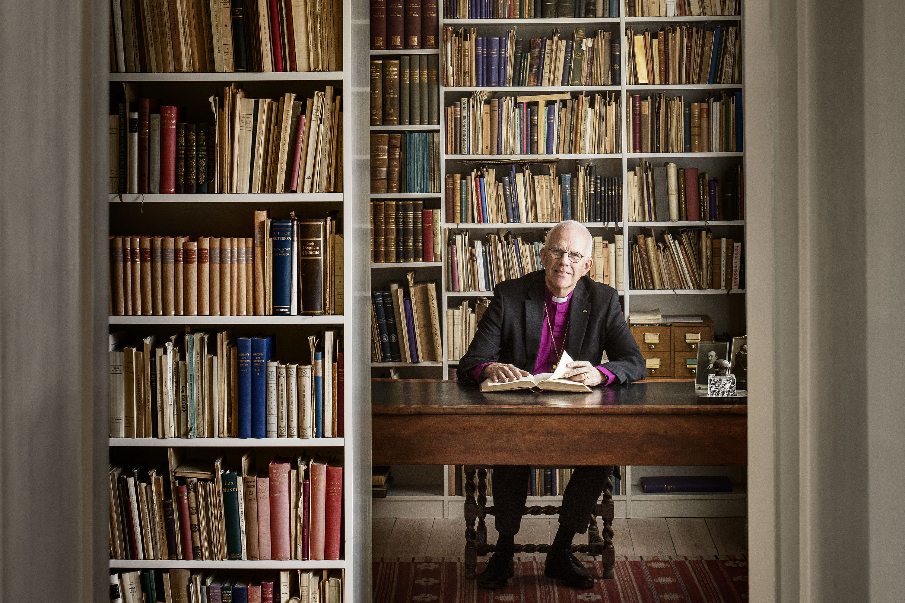 Ärkebiskop Martin Modéus sitter vid skrivbordet framför en bokhylla som täcker väggen.