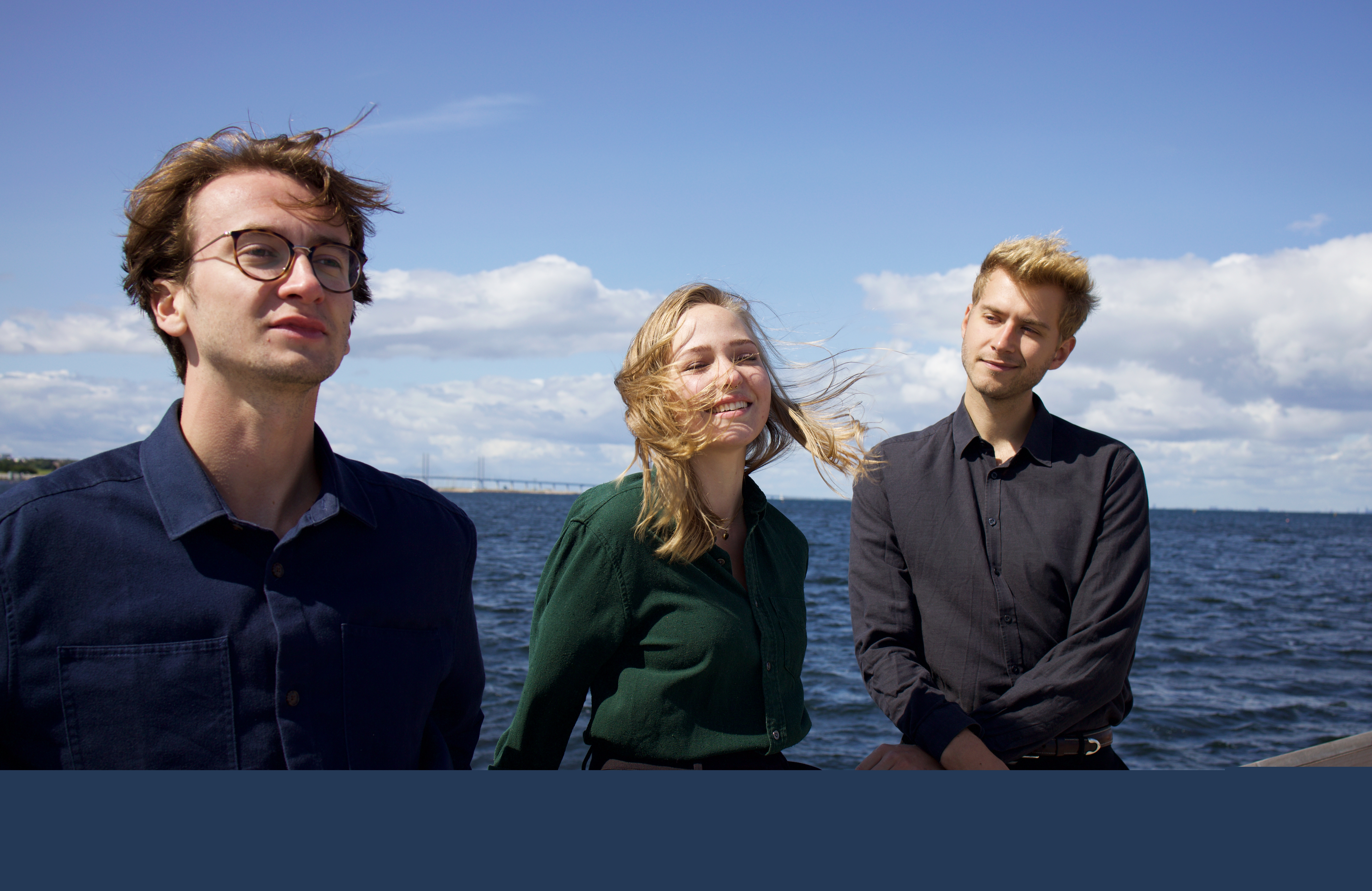 Tre personer vid havet. Himlen är blå.