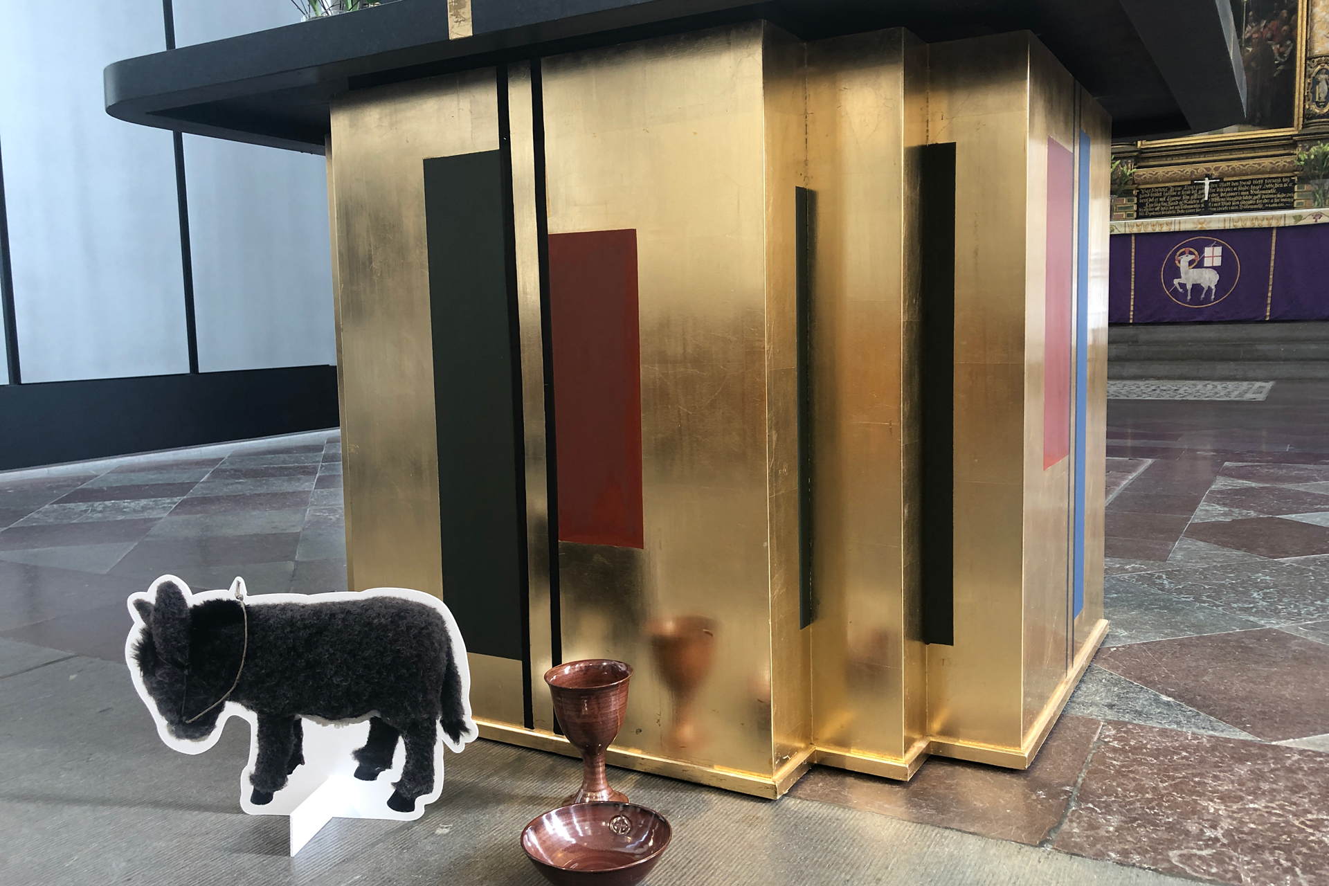 Åsna i papp på stengolv framför altare i guld.