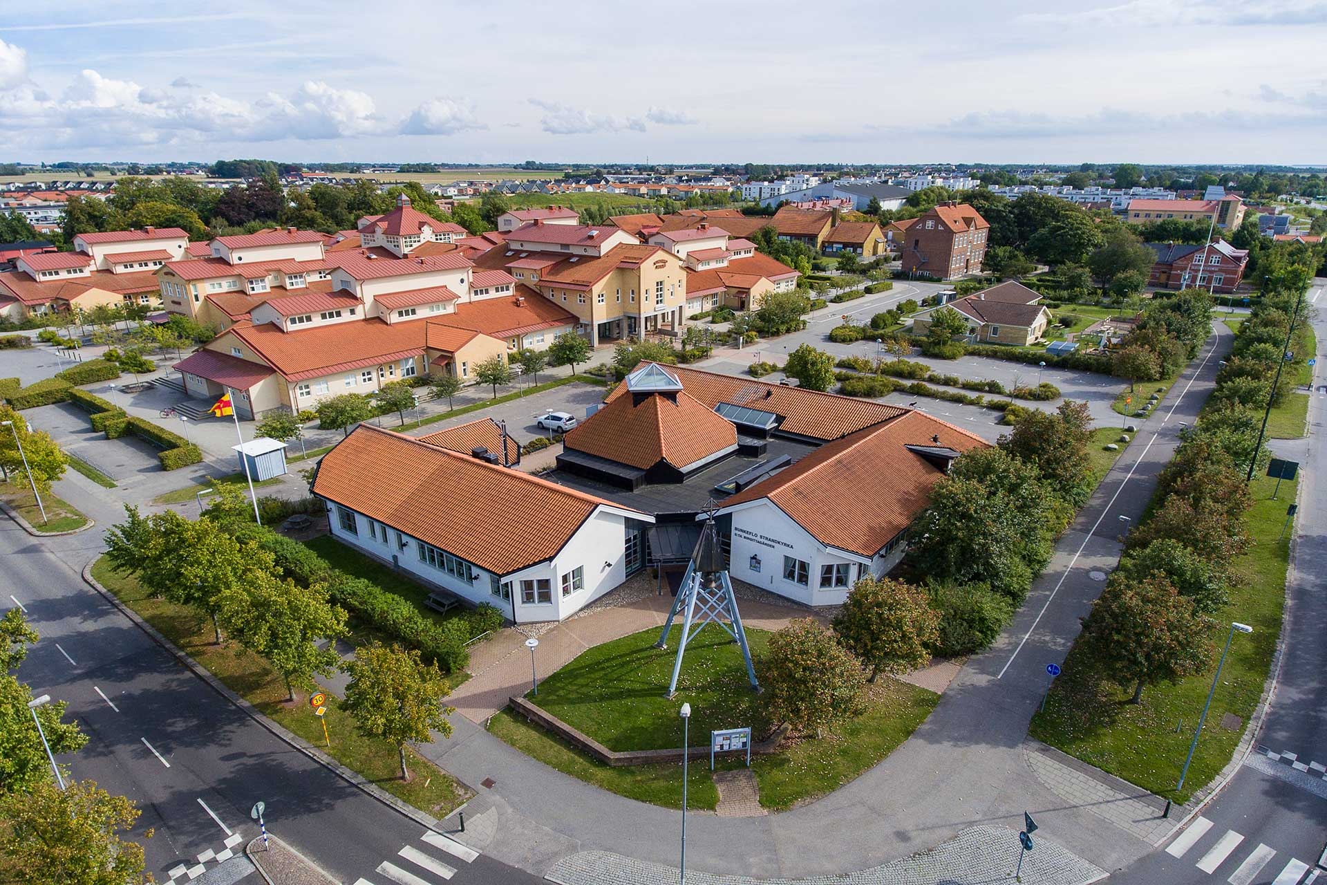 Flygbild över Bunkeflo Strandkyrka, en vit trelängad byggnad med rött tegeltak.