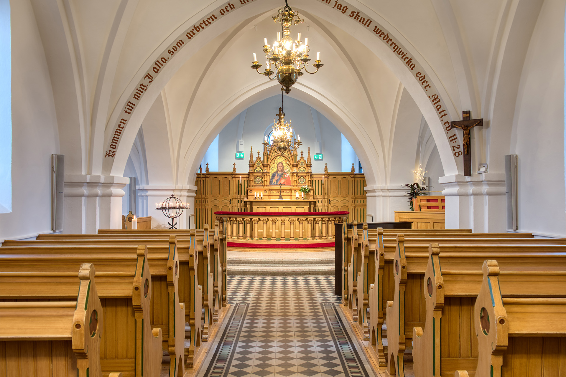 Kyrkgång med kyrkbänkar och altare i bakgrund.