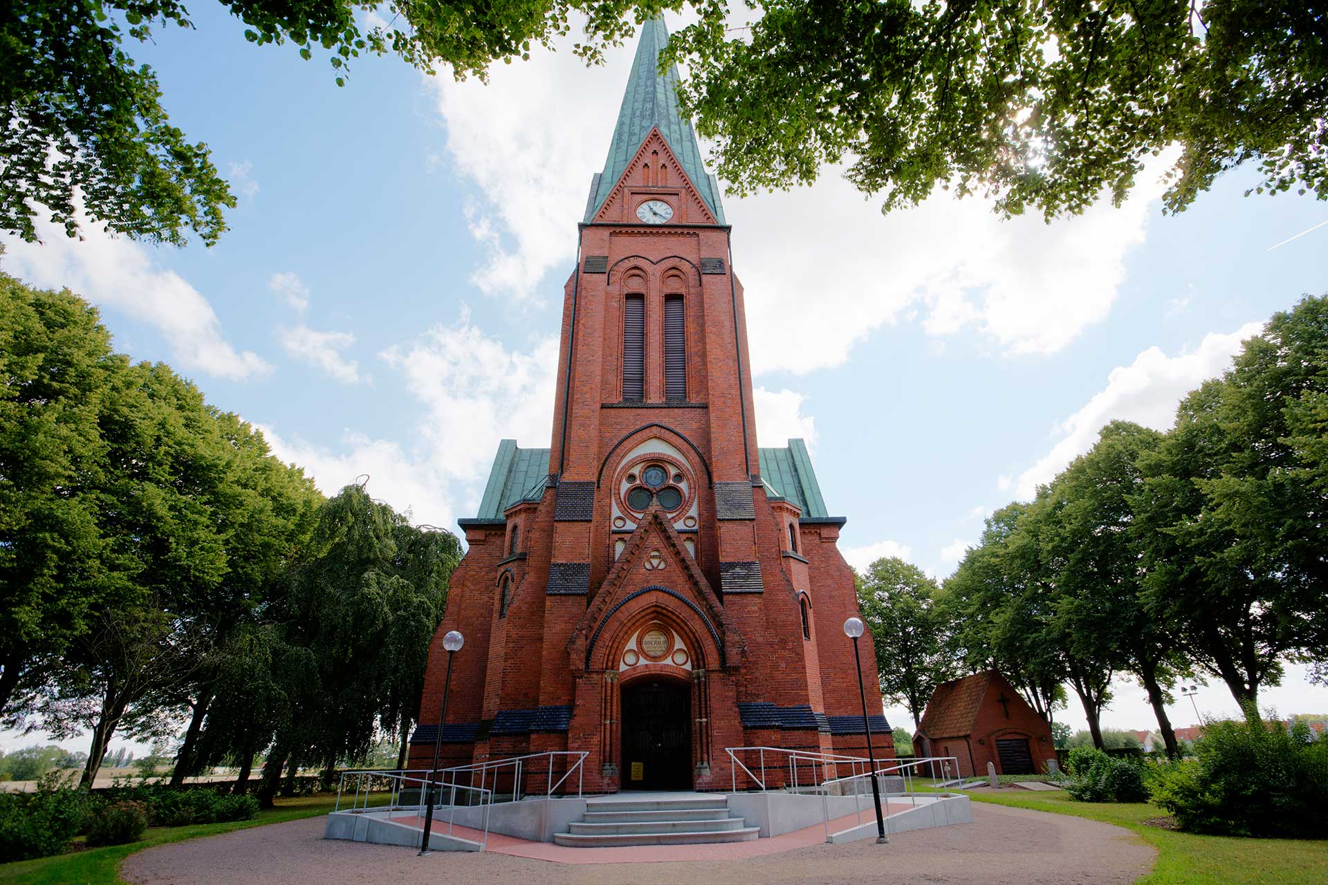 Röd tegelkyrka omgiven av träd.
