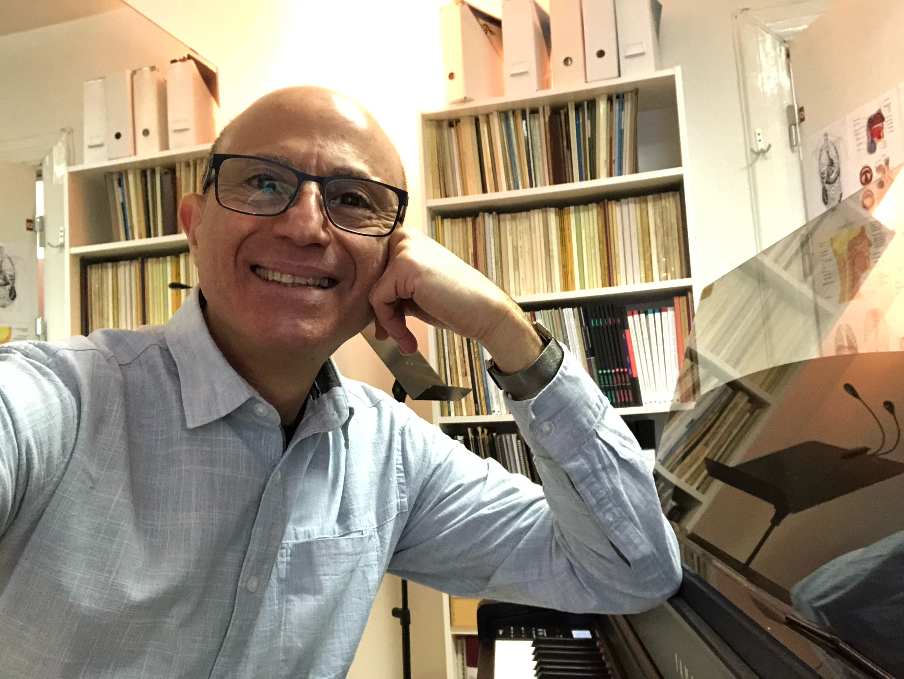 Medelåldersman som lutar armbågen mot ett piano och vilar kinden mot den knutna handen.