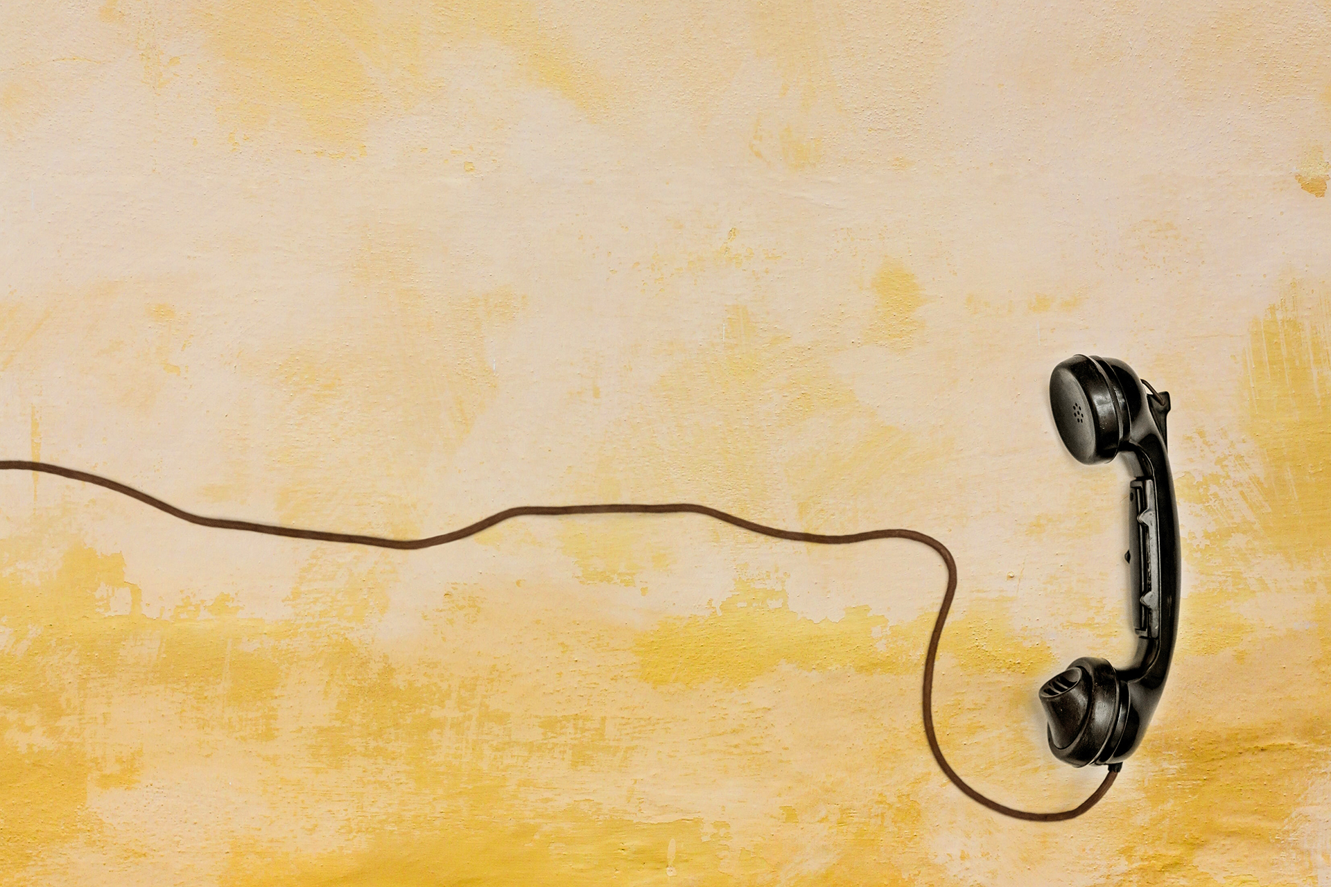 En gammal telefonlur med sladd mot en ljusgul bakgrund.
