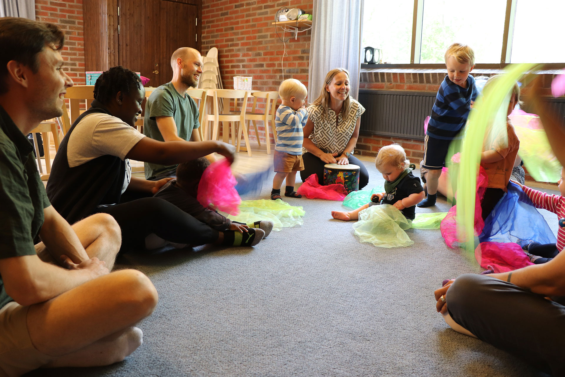 Föräldrar och barn sitter i en ring och viftar med sjalar i olika färger.