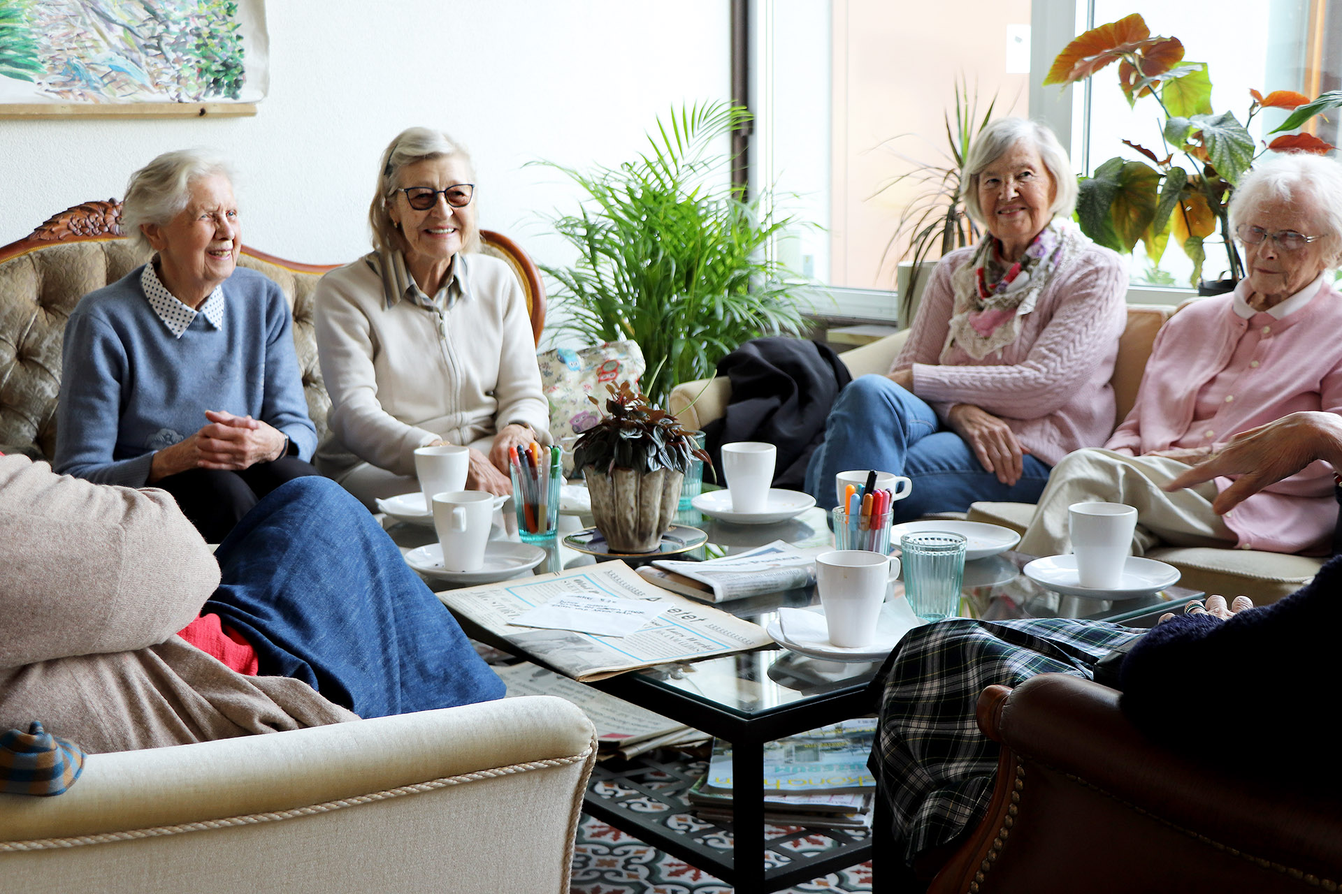 Äldre kvinnor samtalar runt ett bord med kaffekoppar.