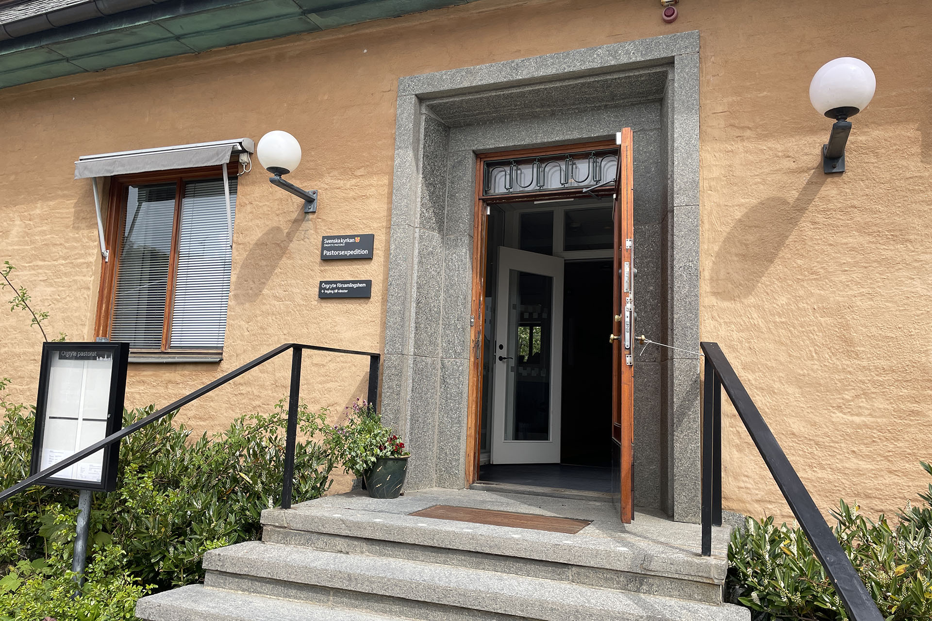 En öppen dörr i ett gult hus med trappa framför.