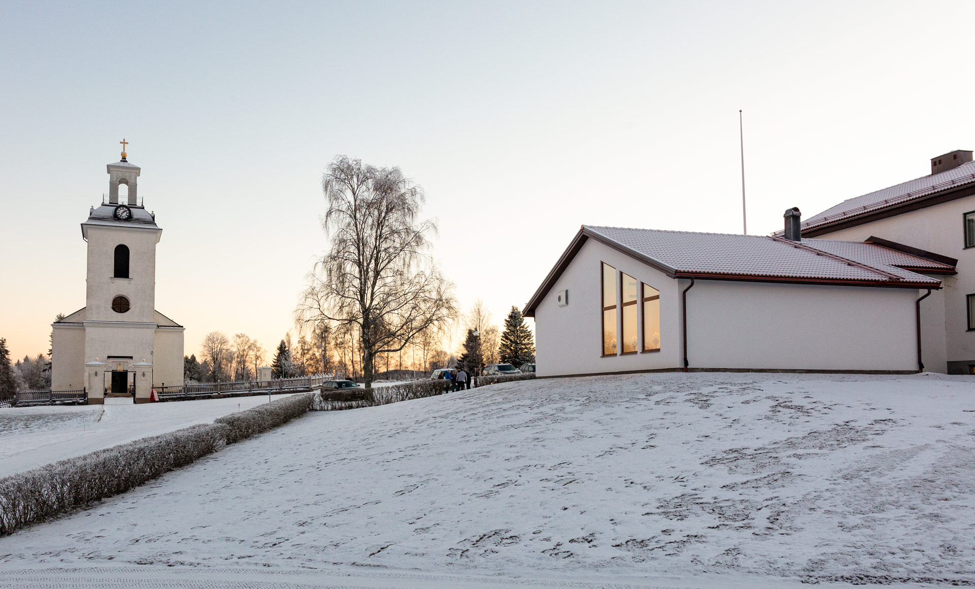 En vy där man ser både Helgums kyrka, till vänster, och begravningskapellet till höger. Ett tunt snötäcke ligger över mark och byggnader.