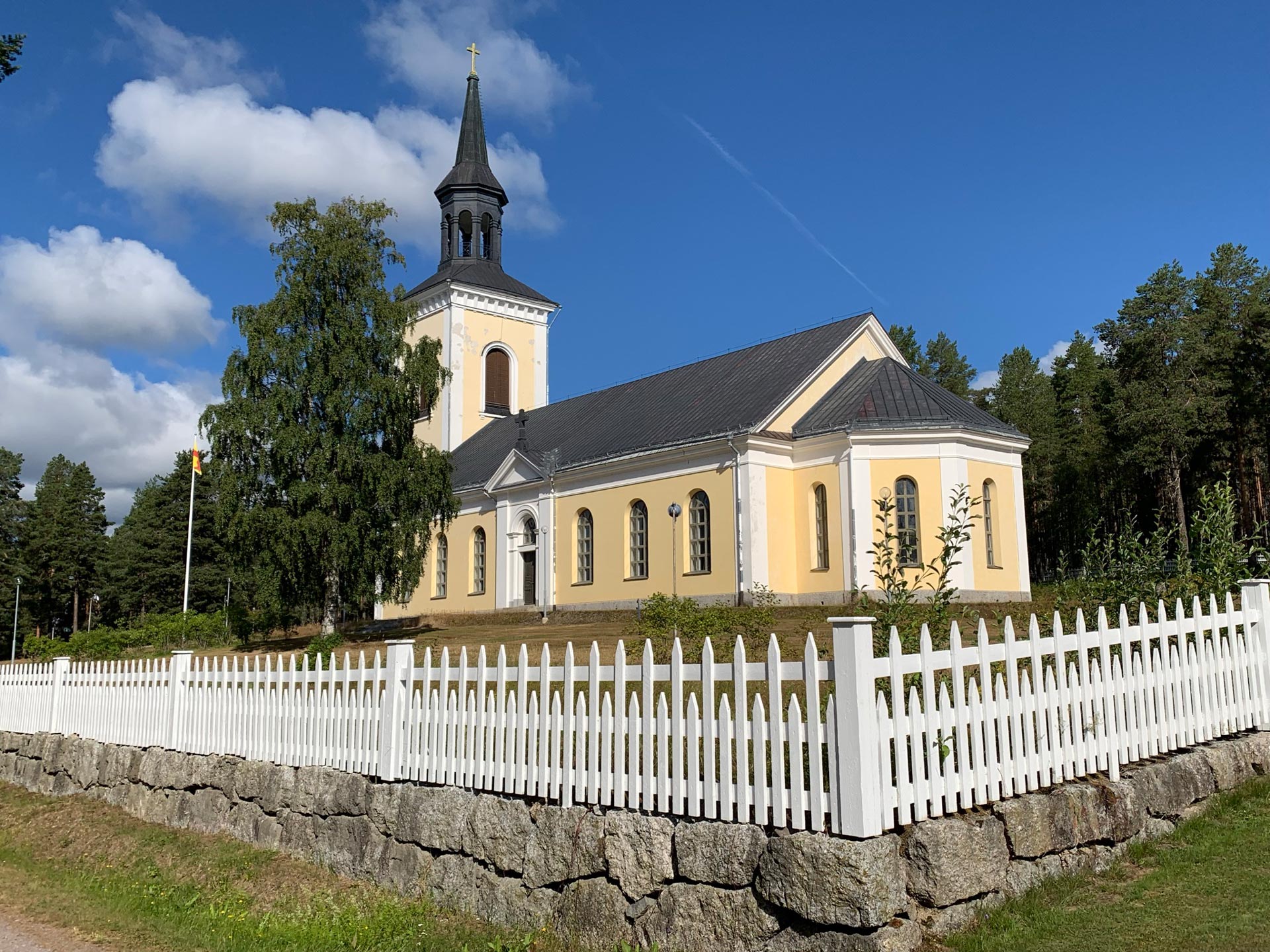 Gulrappad kyrka. I förgrunden ett vitt trästaket.