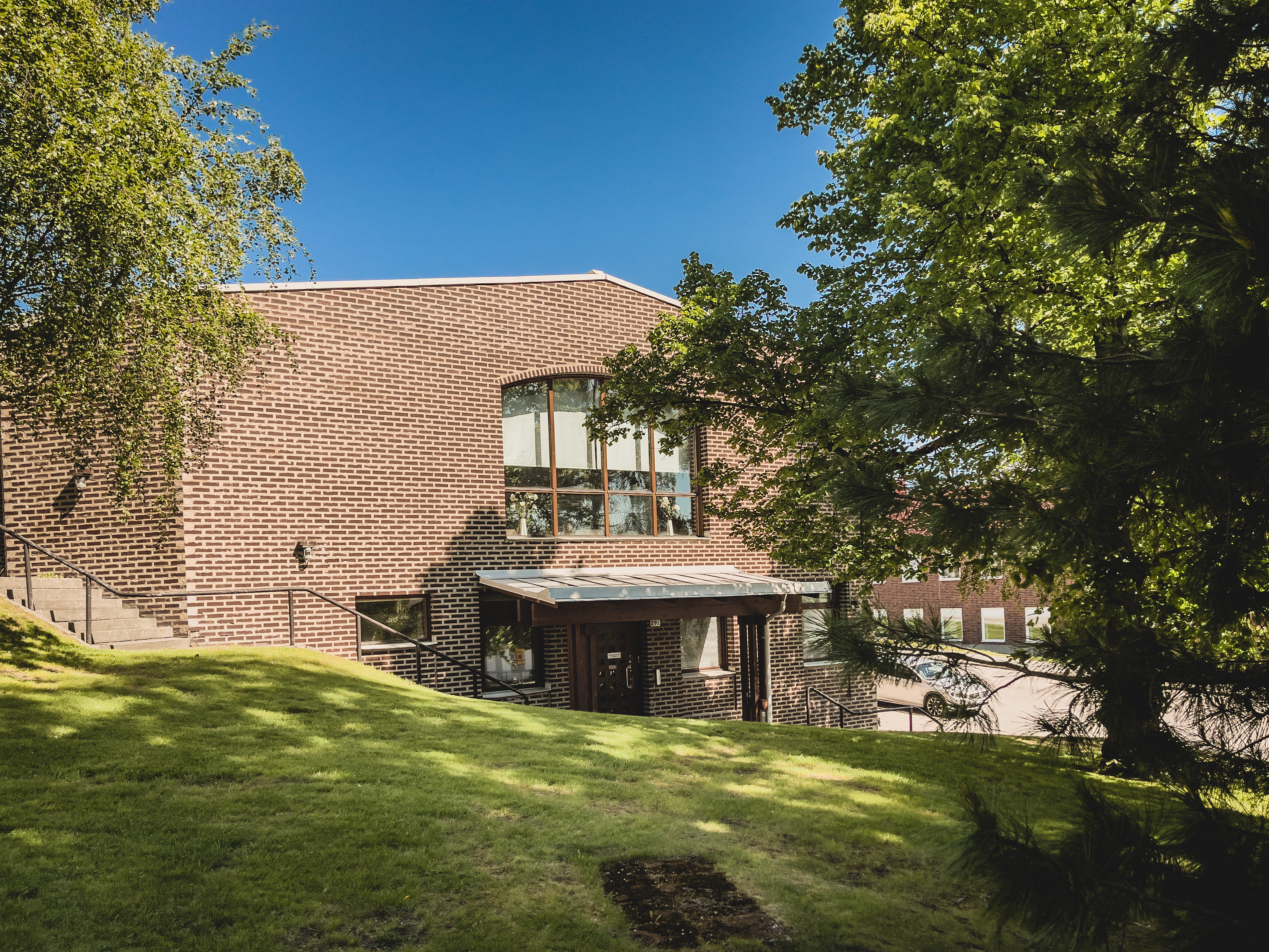 Sidobild på en stor tegelbyggnad. Träd i förgrunden