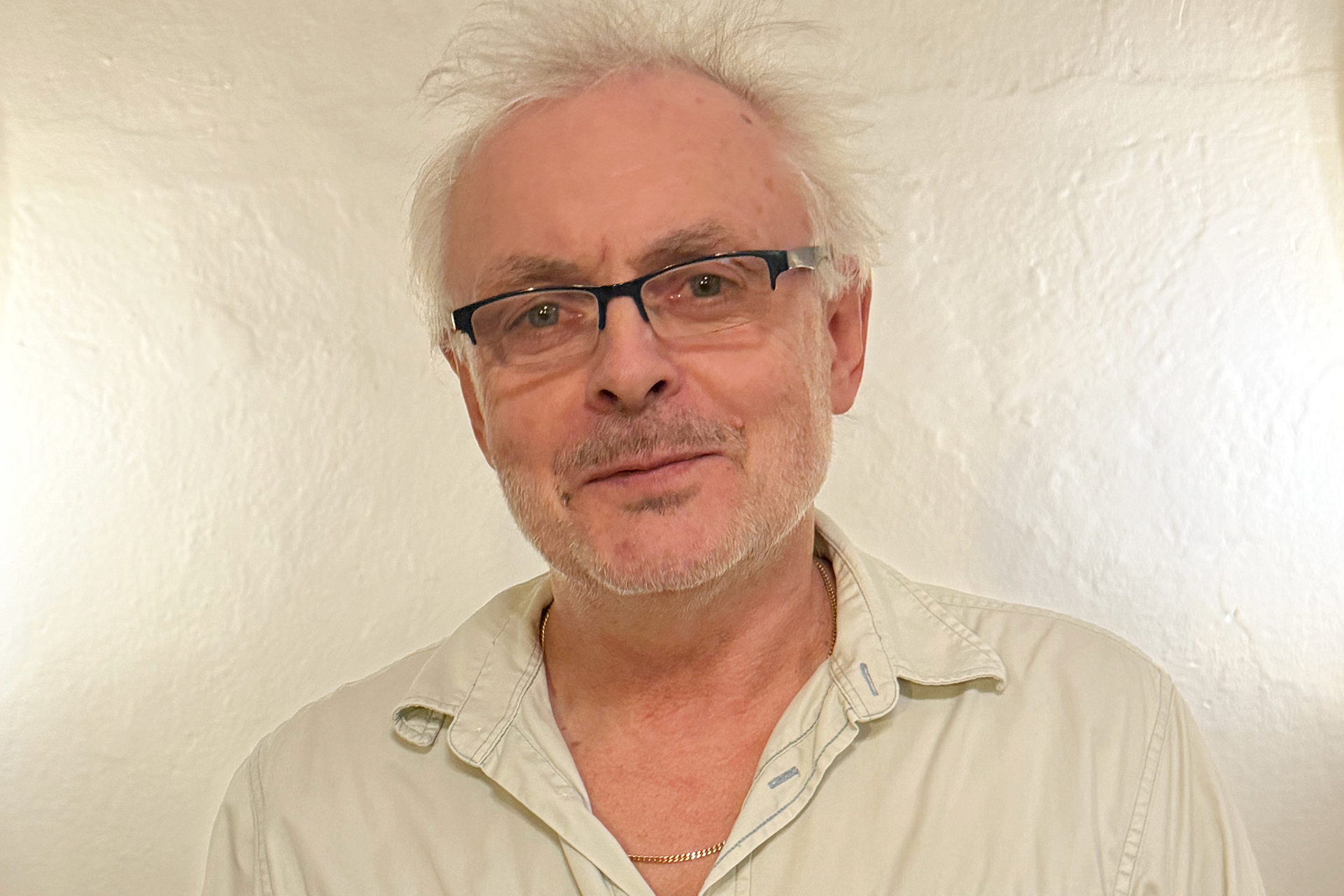 Man i ljus skjorta och glasögon framför en kalkputsad vägg.