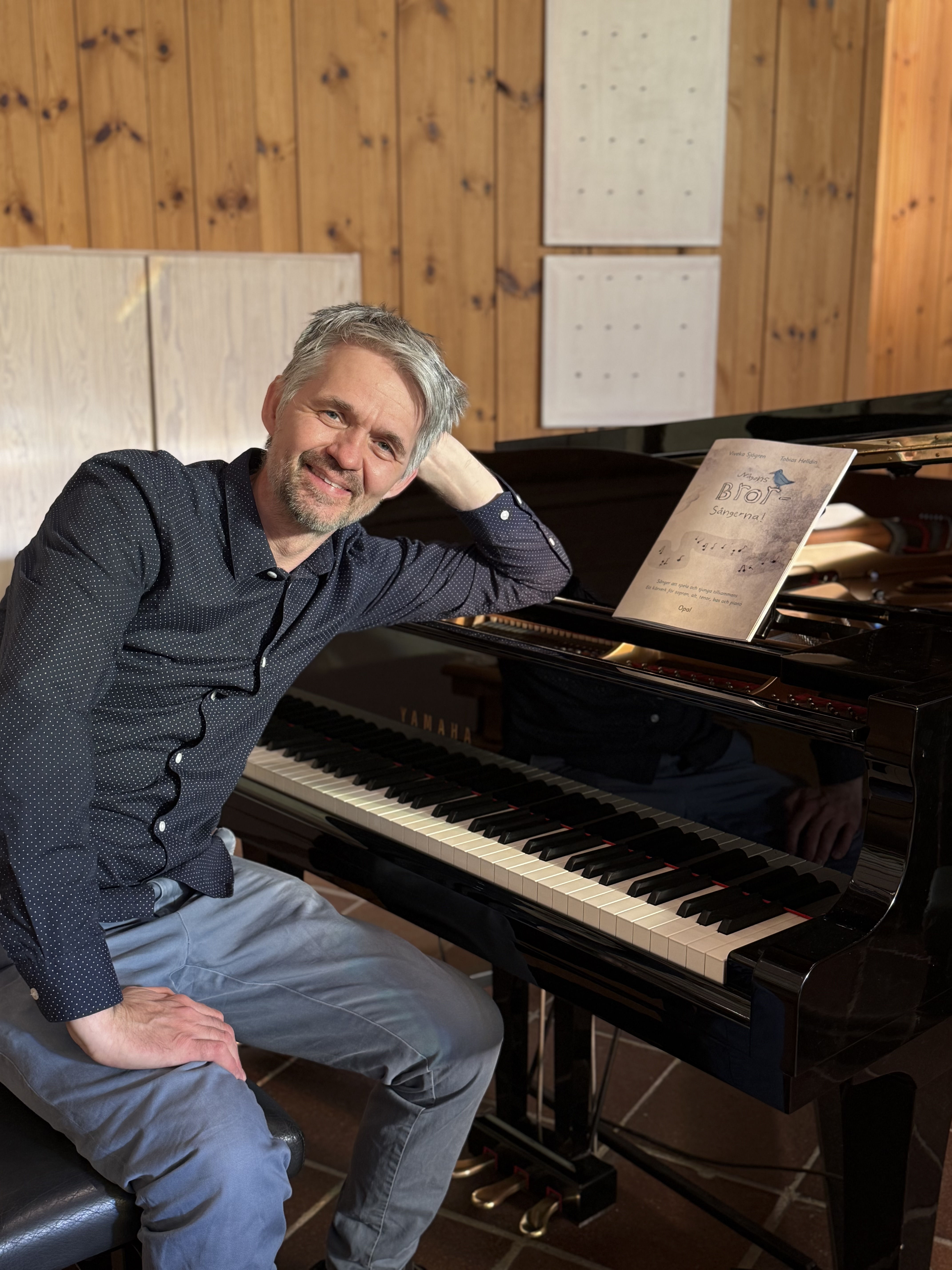 Kyrkomusikern Tobias Helldin lutar sig sittande mot ett piano.