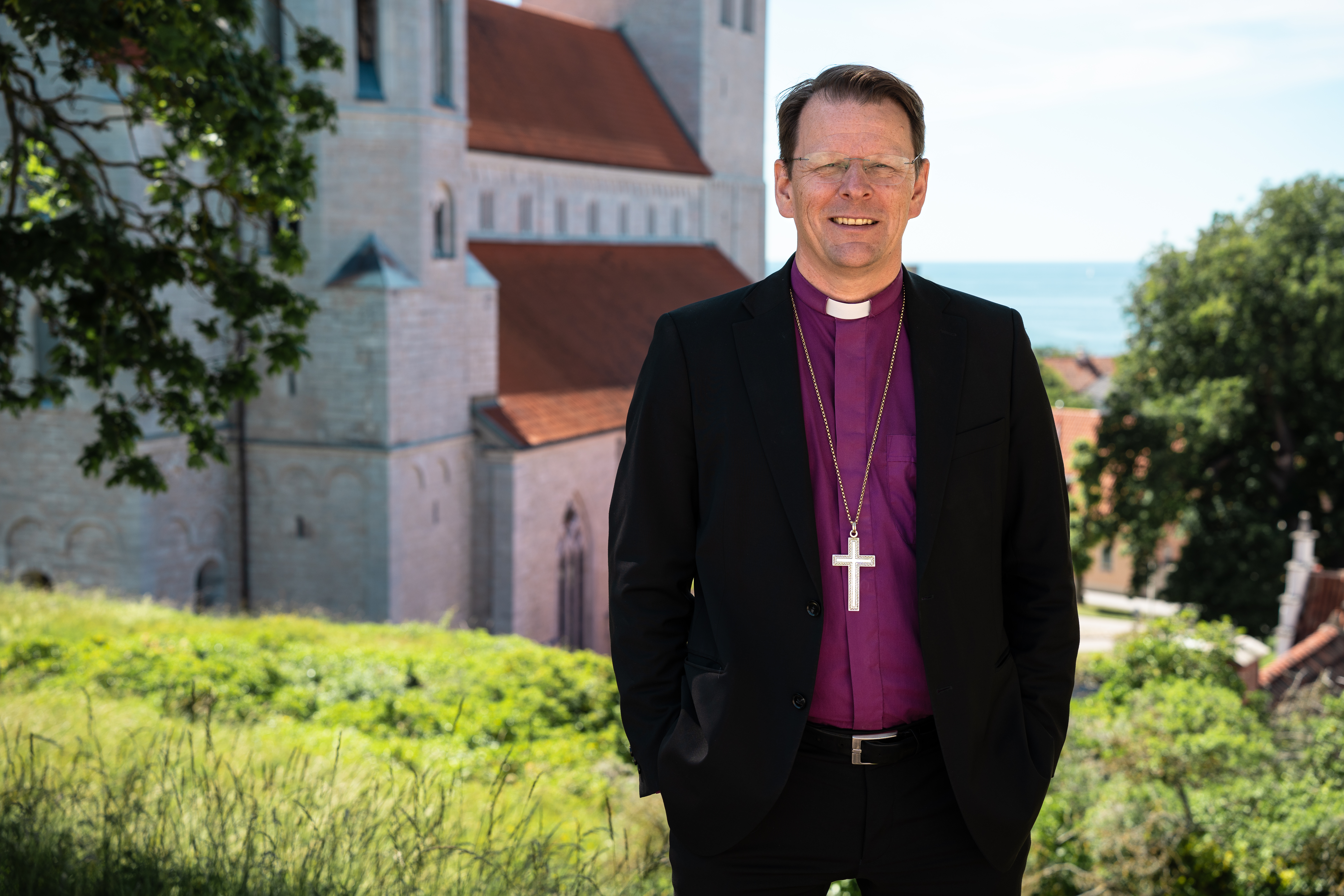 Biskop Erik Eckerdal på klinten ovanför Visby domkyrka med kyrkan och havet i bakgrunden