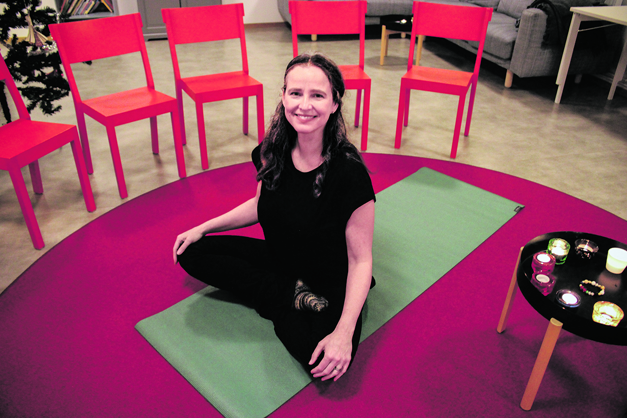 Helena sitter i skräddarställning på en yogamatta