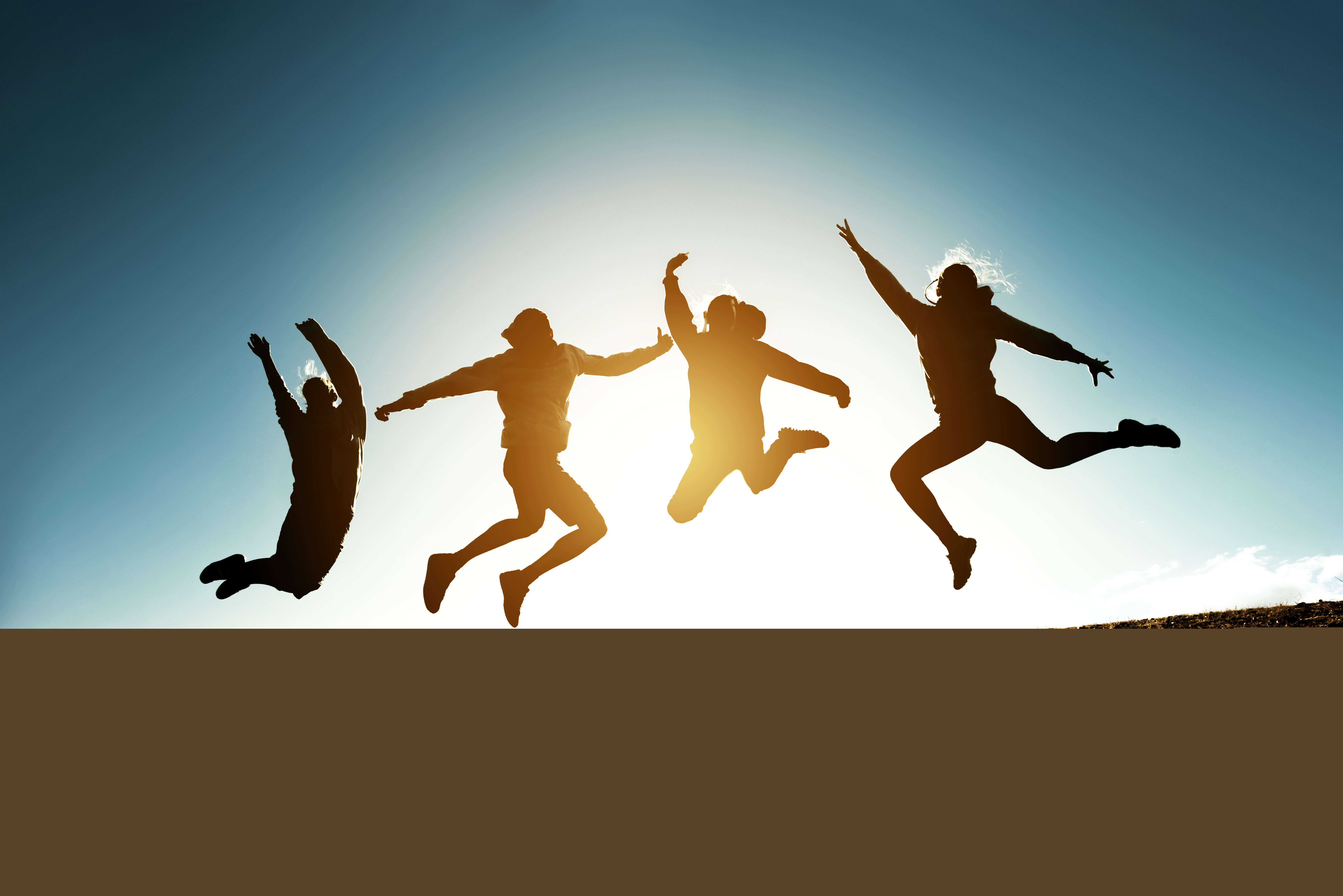 Tonåringar som hoppar, de syns enbart som siluetter mot en ljus himmel.