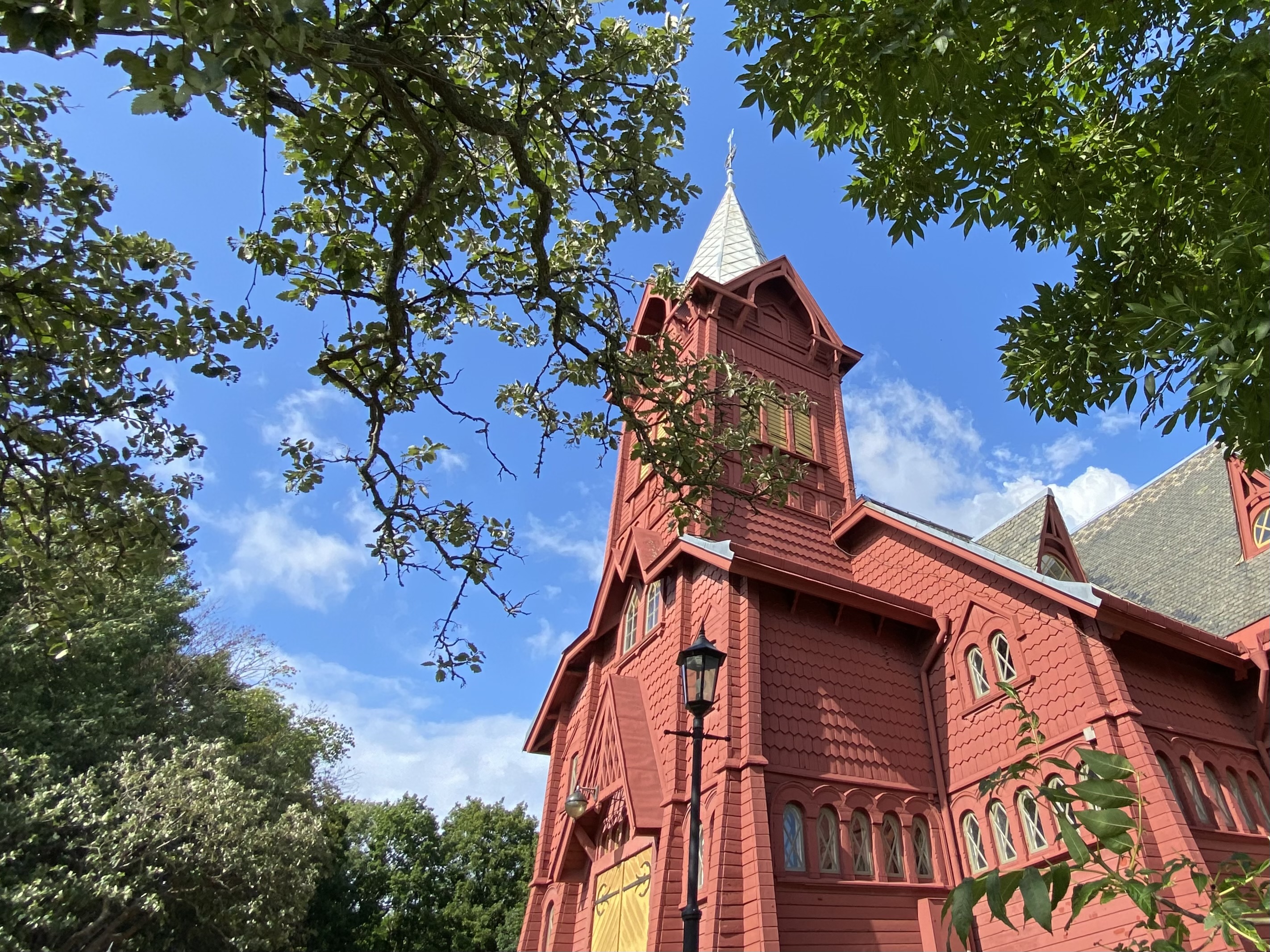 Tornet på Hälleviksstrands kyrka sett underifrån genom grönt lövverk.