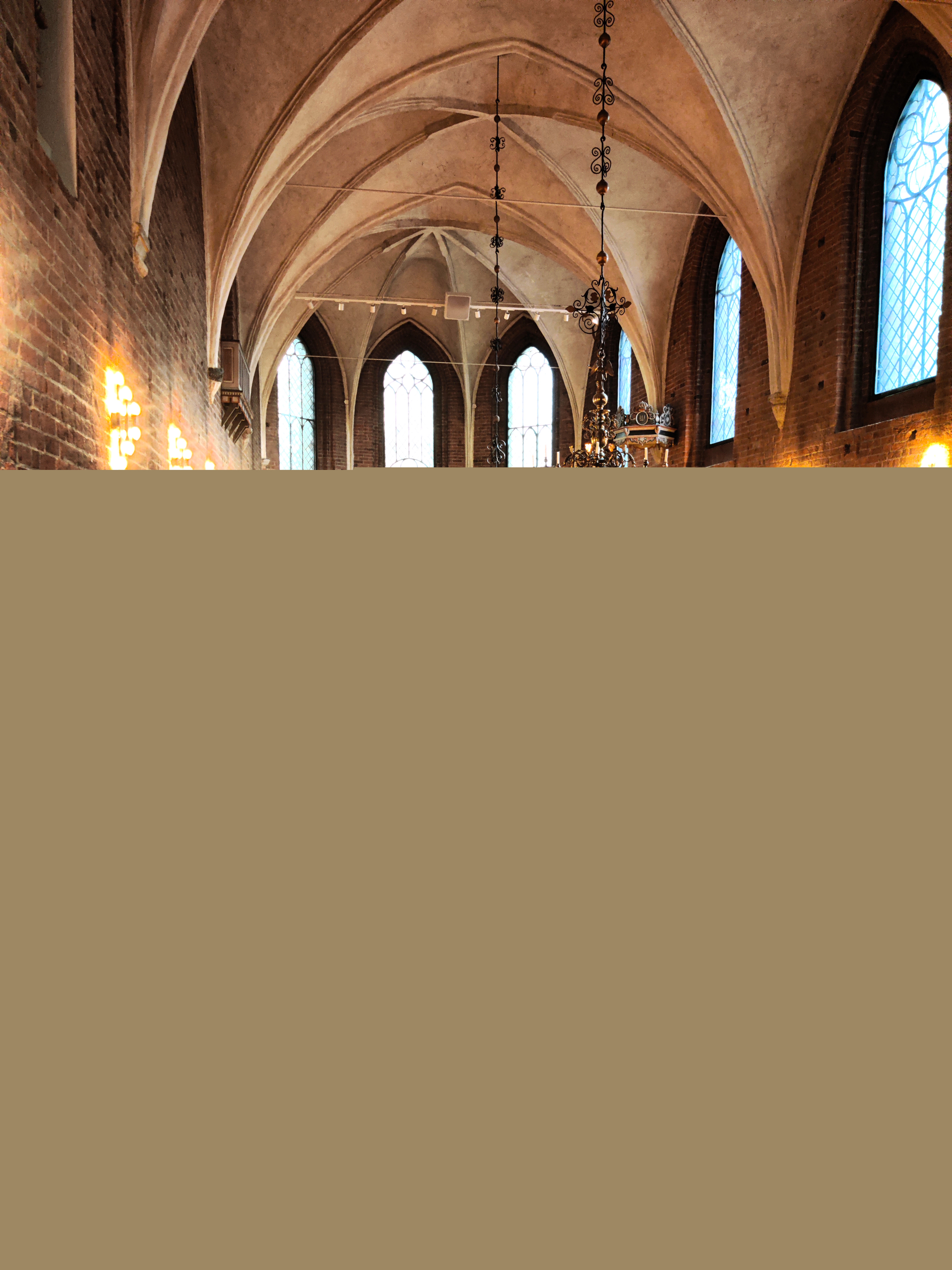 Bild tagen inne i kyrkan. Längst bort syns koret med sin altartavla som är belyst. I förgrunden syns ljusbäraren samt bänkraderna.   