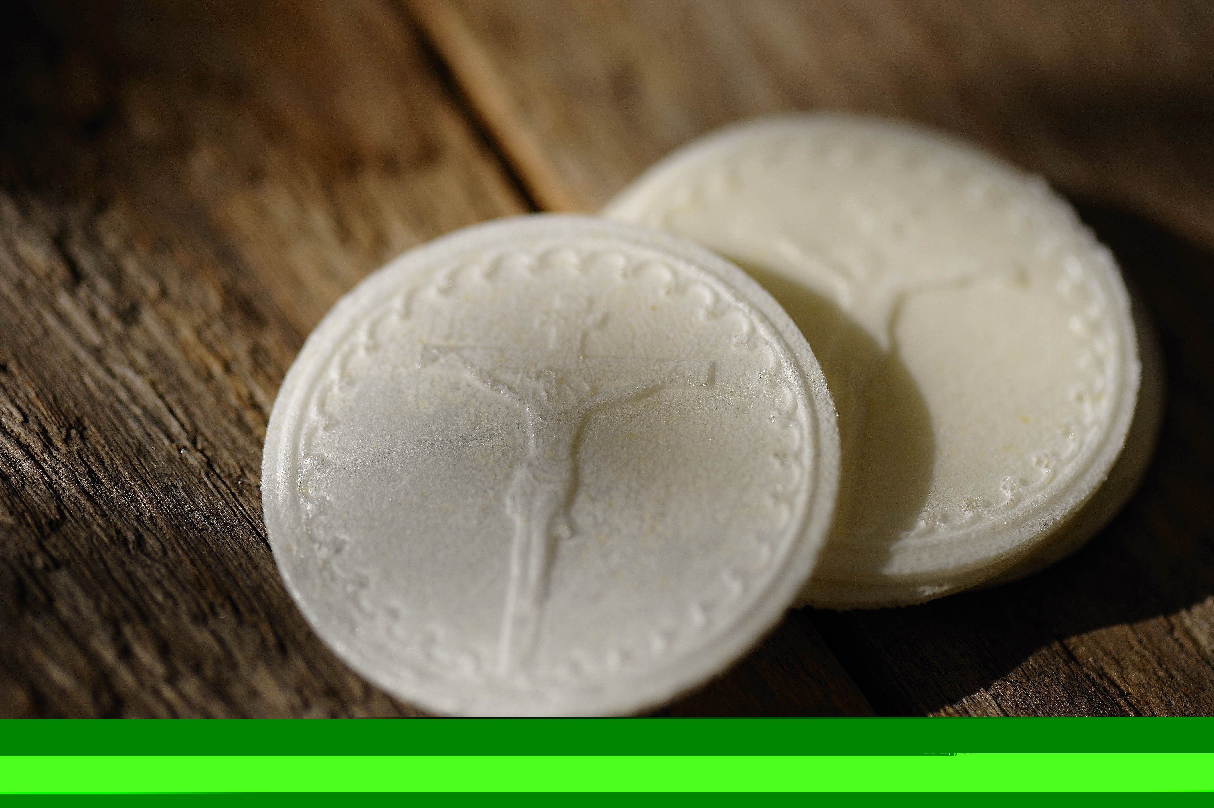 Två oblater ligger på ett bord. På det övre oblatet ser man Kristus på korset.