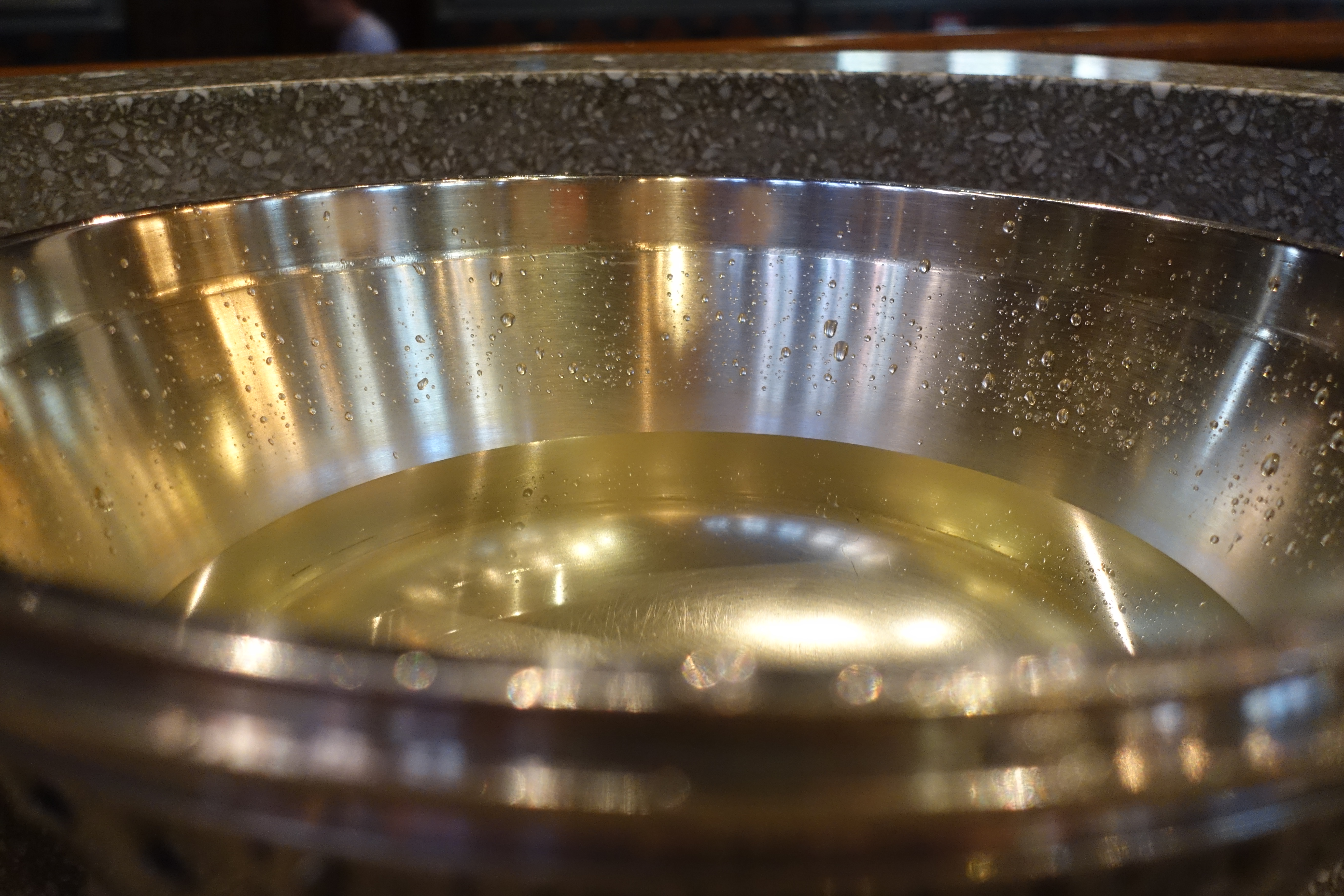 Närbild på dopskål i silver med vatten i och vattendroppar på kanten.