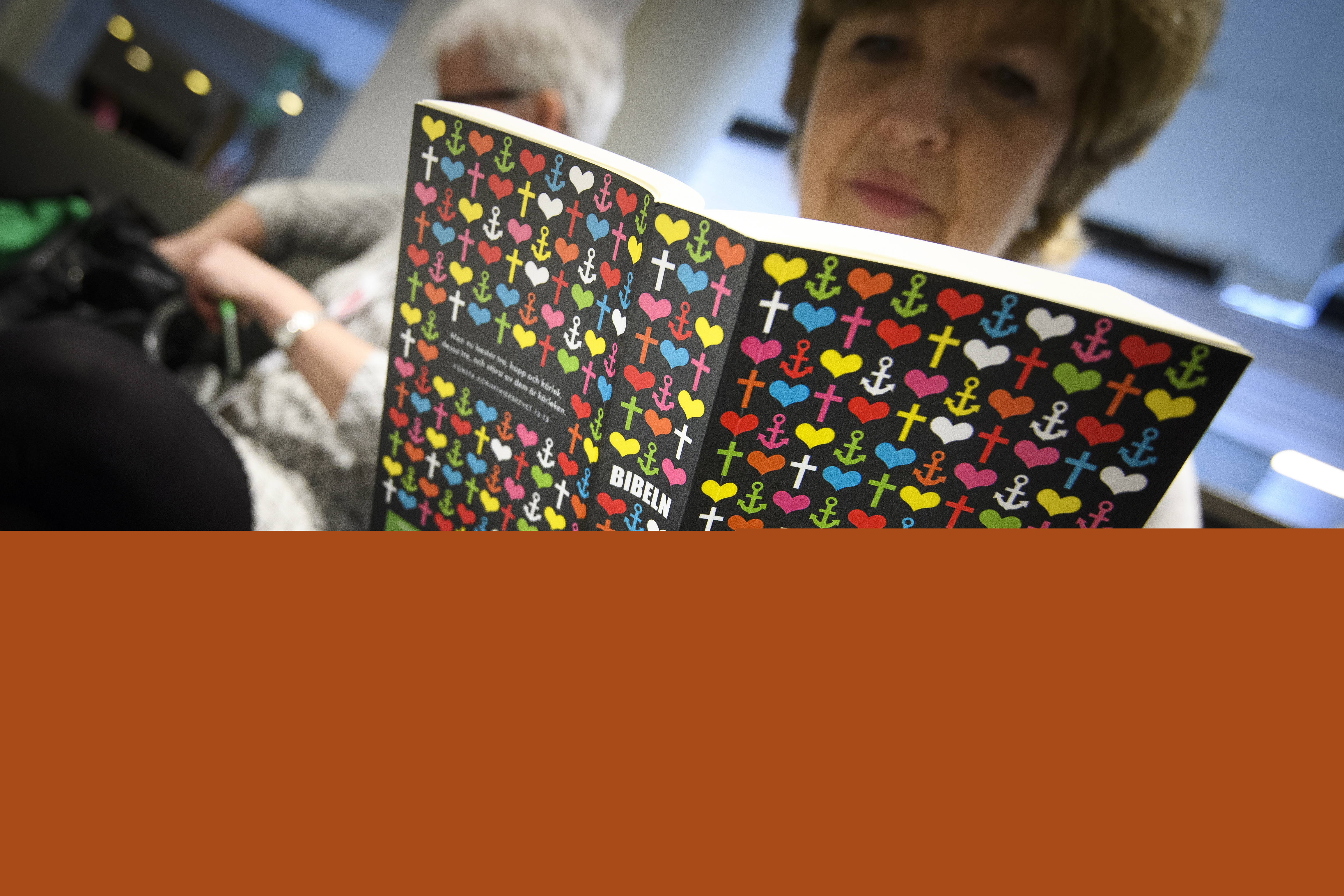 En kvinna sitter och läser Bibeln. I bakgrunden syns en kvinna till. 