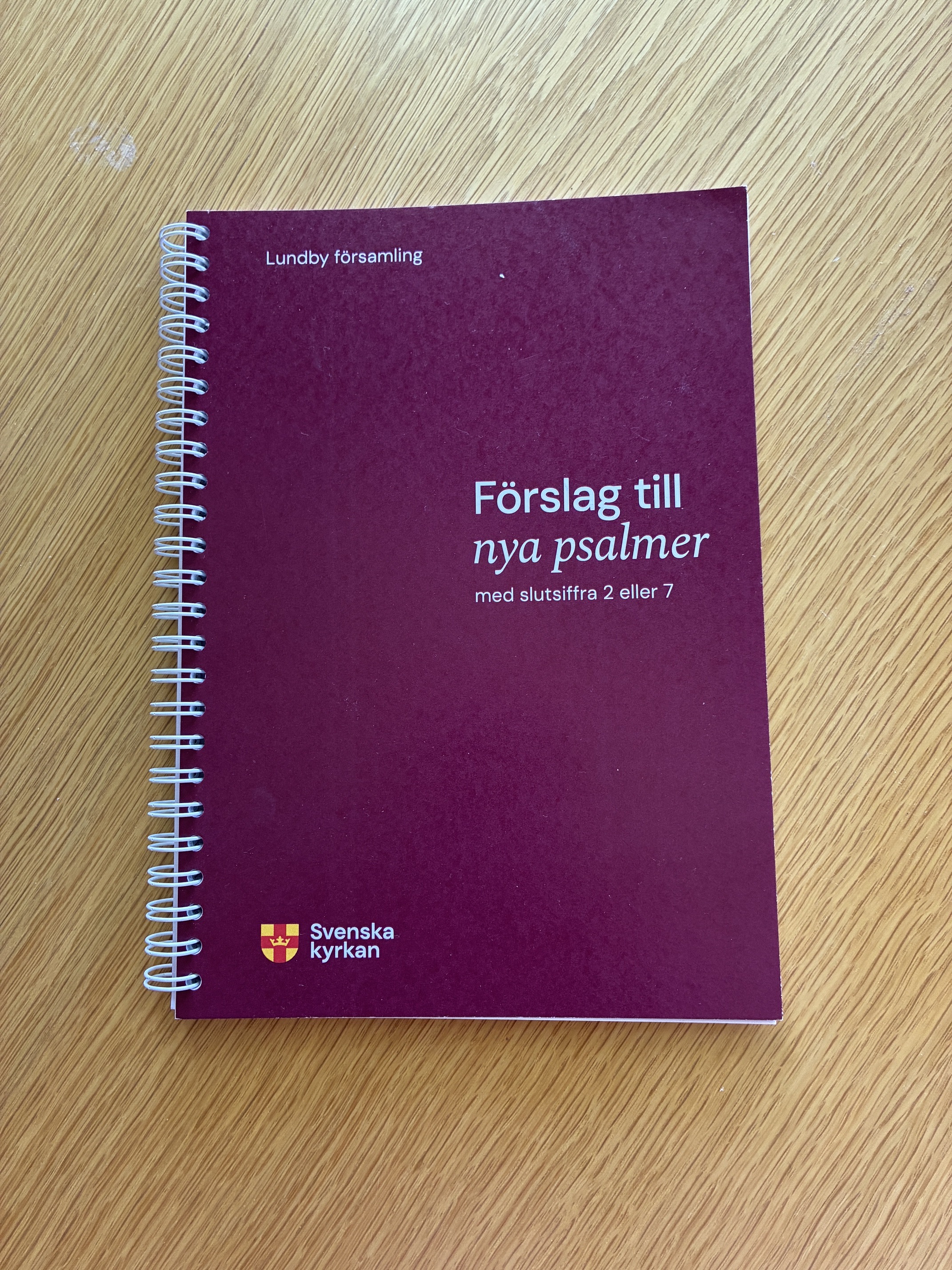 En bok med spiralbindning. På boken står det "Förslag till nya psalmer med slutsiffra 2 eller 7" Lundby församling.