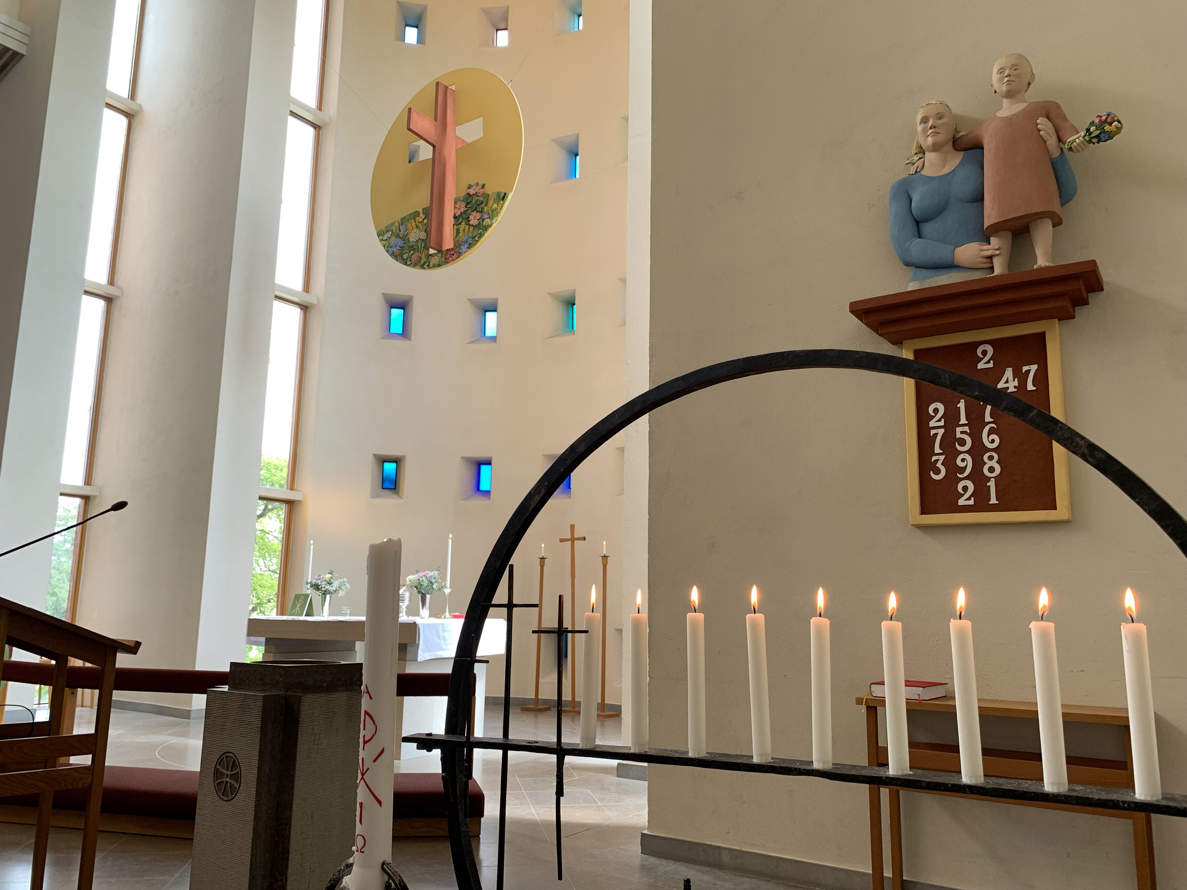 Ett ljust och modernt kyrkorum. I förgrunden syns en ljusstake med sju brinnande ljus och ett större Kristusljus. I bakgrunden står kyrkans altare dukat för nattvard.