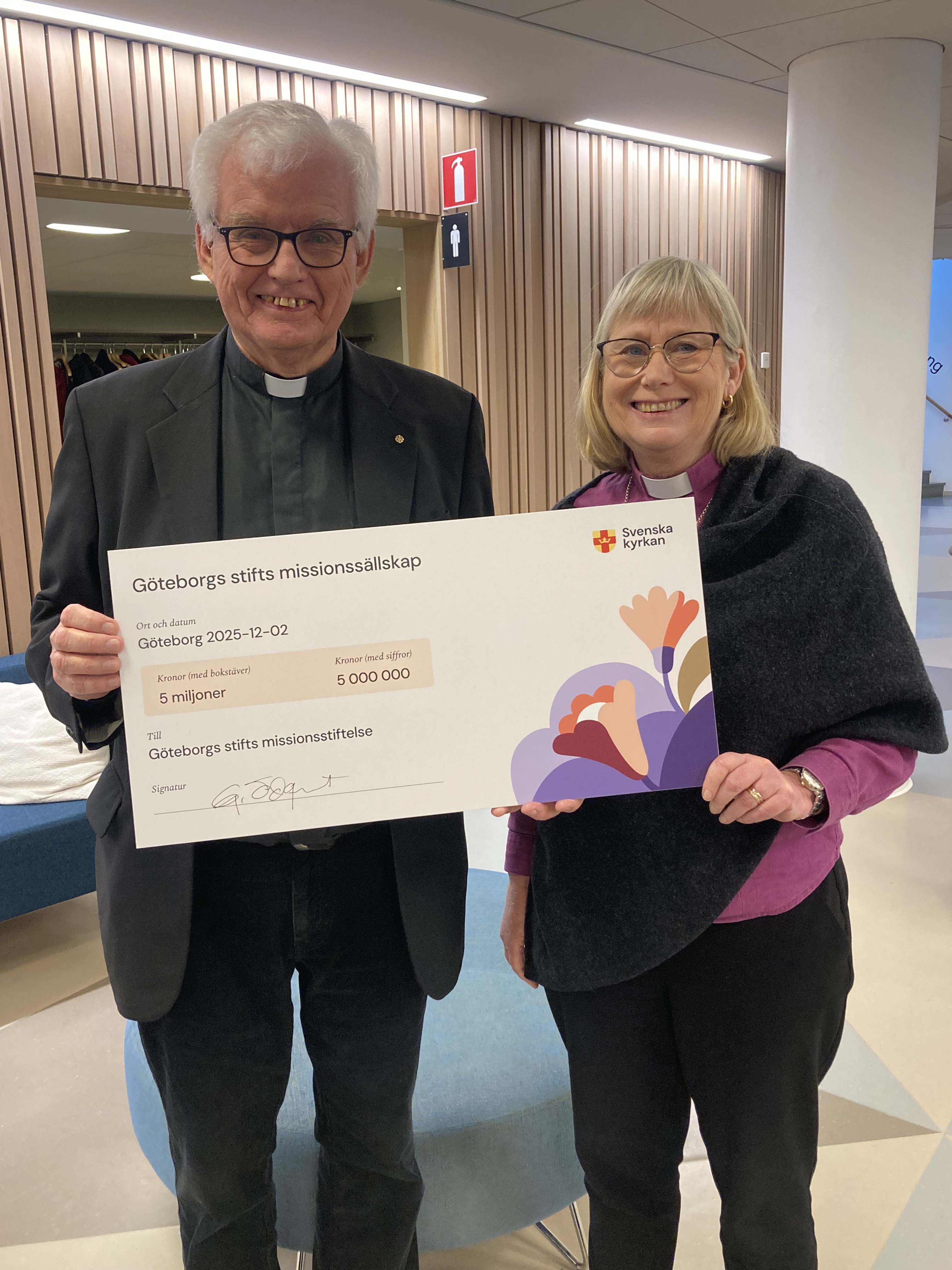 Biskop Susanne tar emot en check på fem miljoner av Göteborgs missionssällskaps ordförande Gustav Ödquist. 