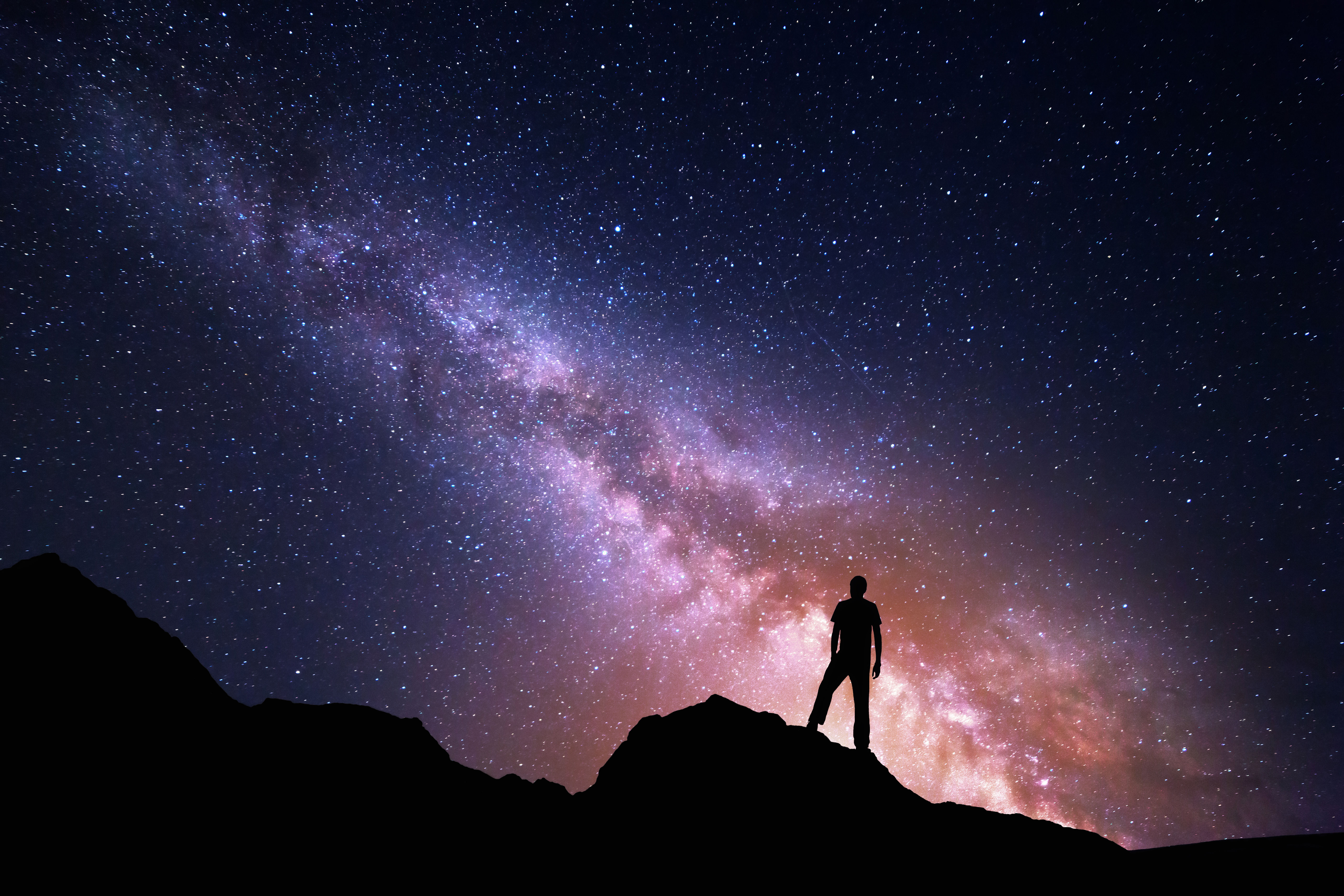 Person står på ett berg och tittar upp på stjärnhimlen