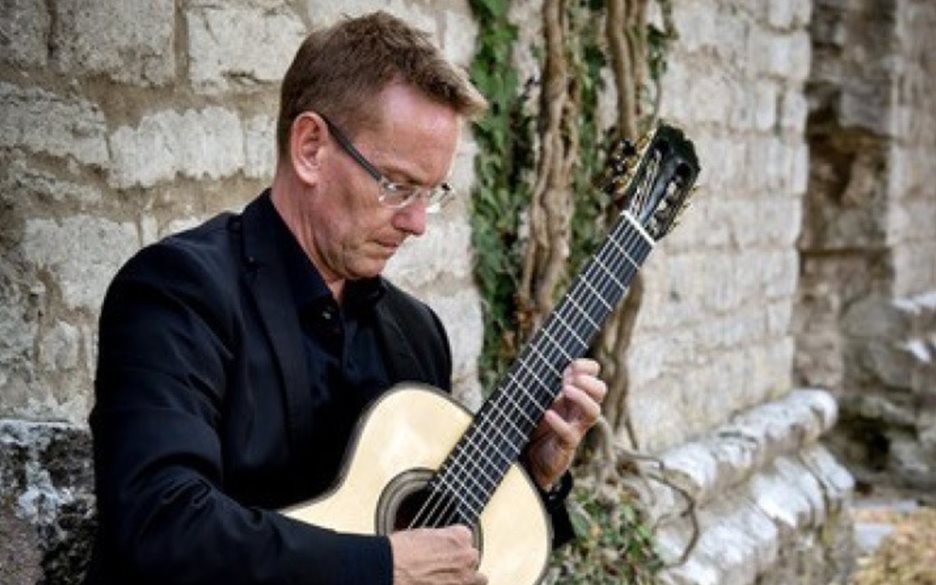 En man sitter framför en stenmur med sin gitarr