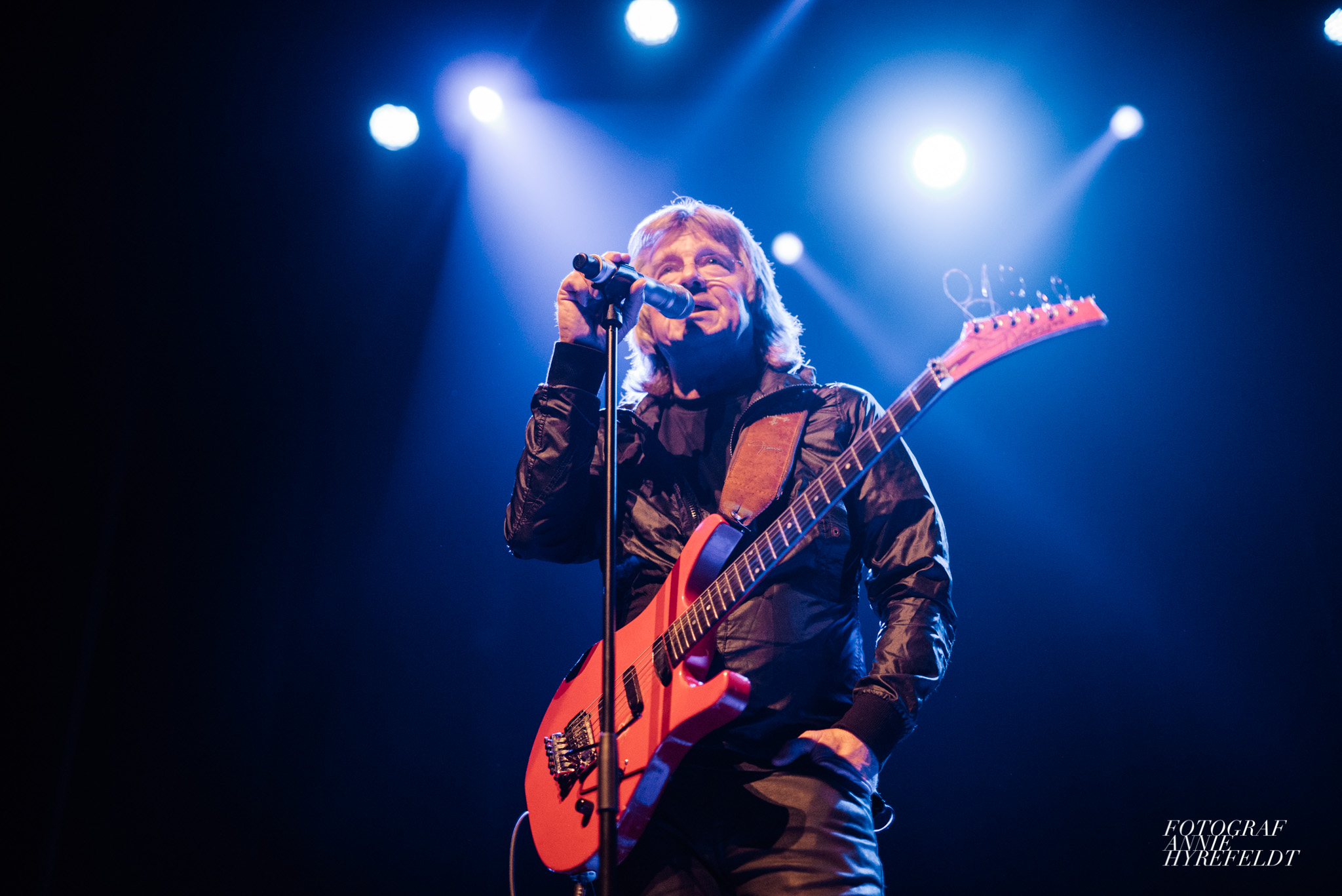 Man sjunger i mikrofon och håller i en röd gitarr.