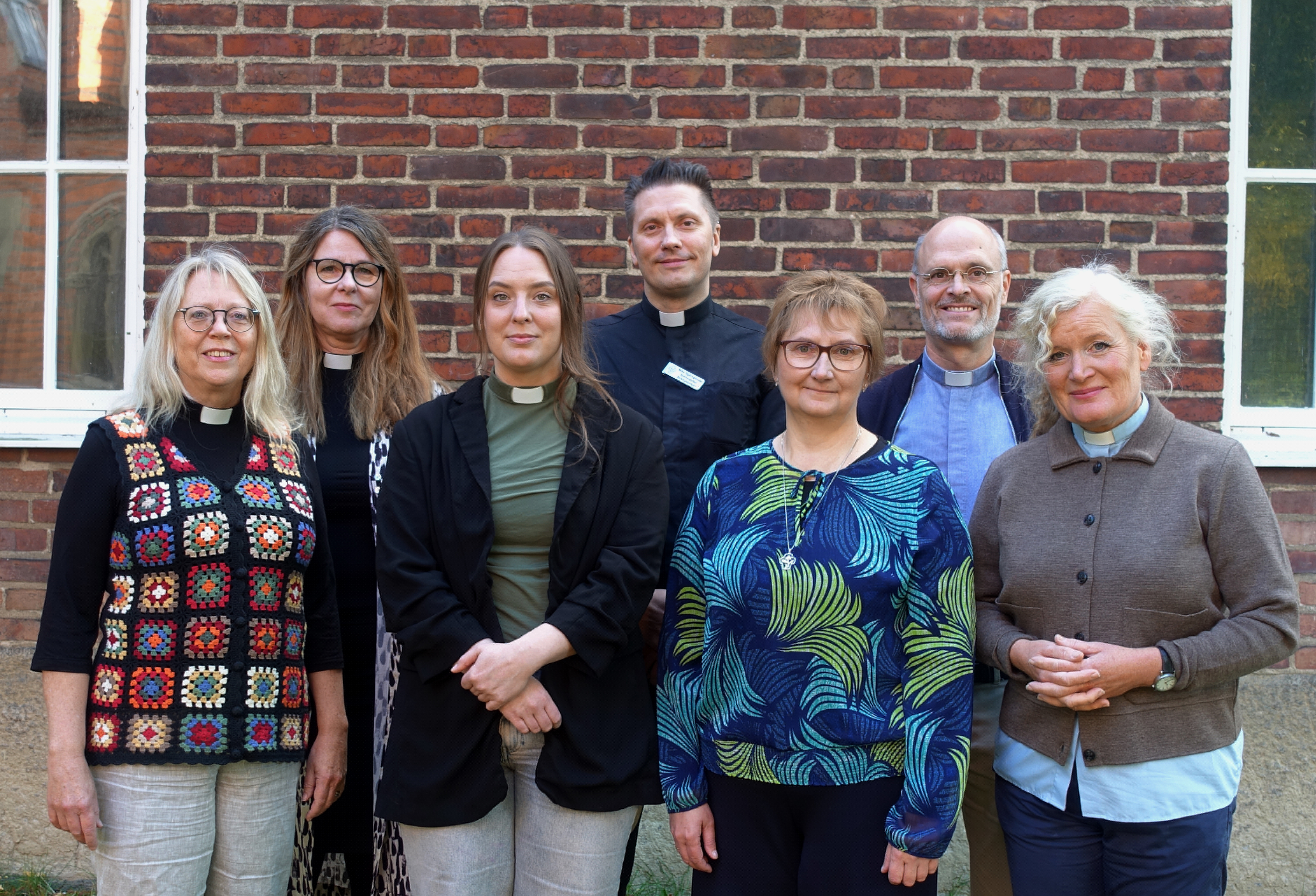 Sjukhuskyrkans personal står i grupp framför en röd tegelvägg.