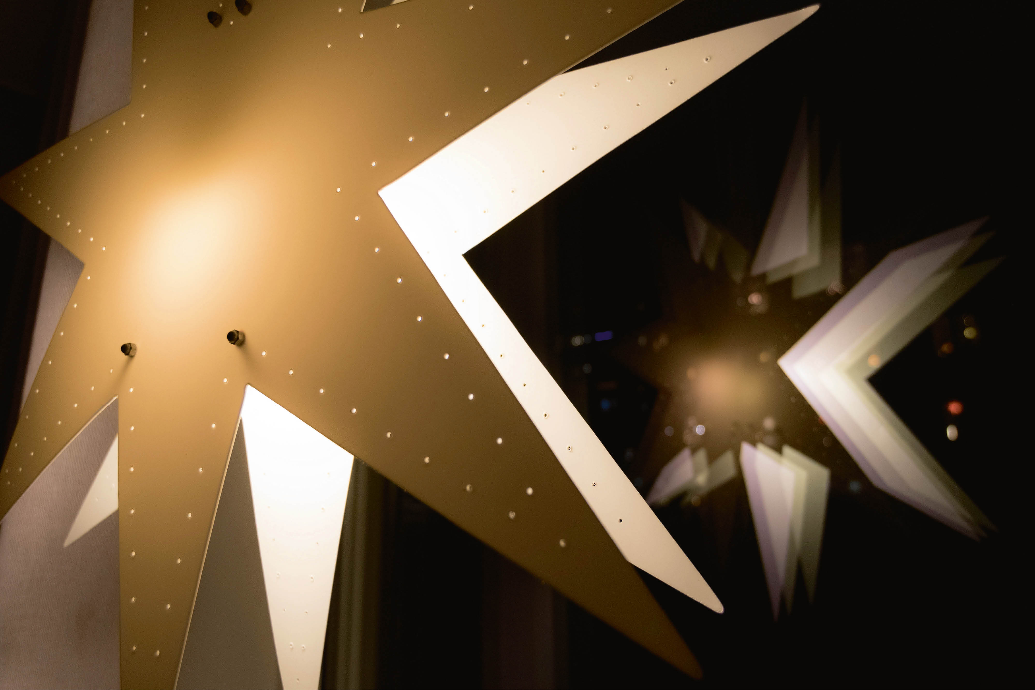 En adventsstjärna i guldpapper hänger i ett fönster. Man ser reflektionen i fönsterglaset.