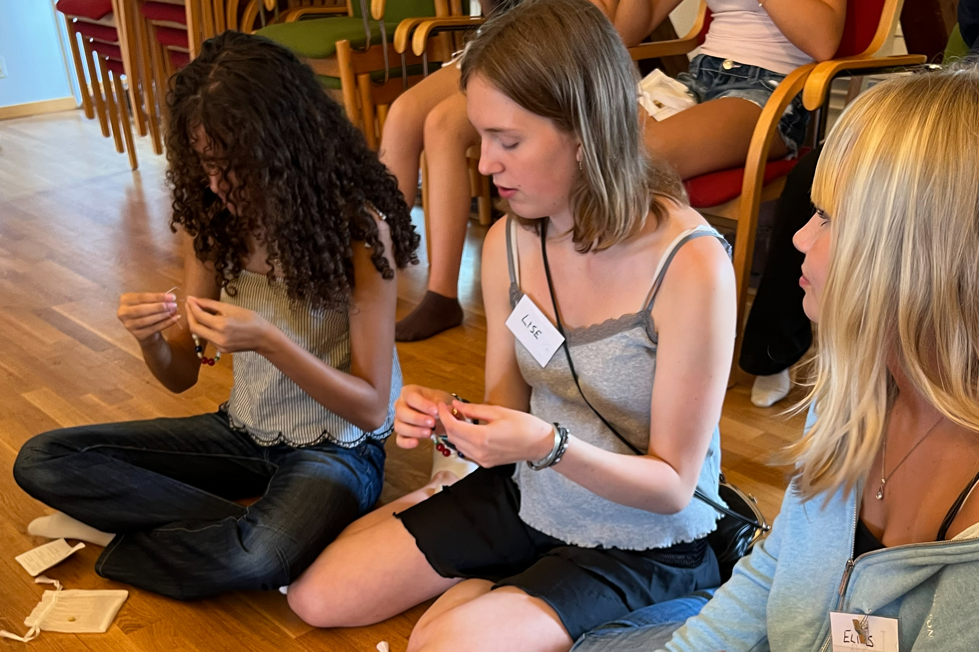 Några tjejer sitter på ett golv med frälsarkransar i händerna.