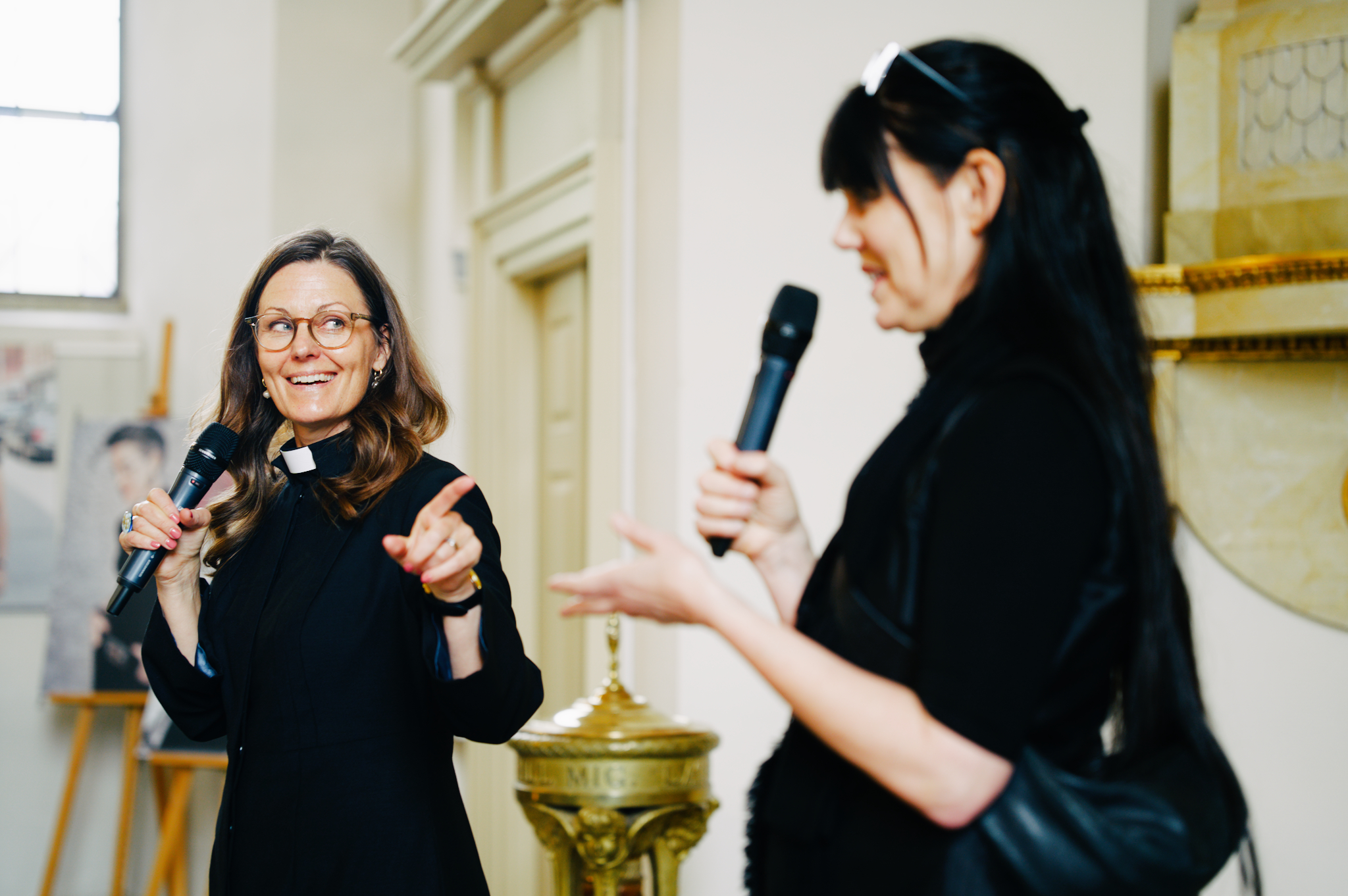Ewa Lindqvist Hotz på scen håller en mikrofon och pekar på en talare som också står på scenen