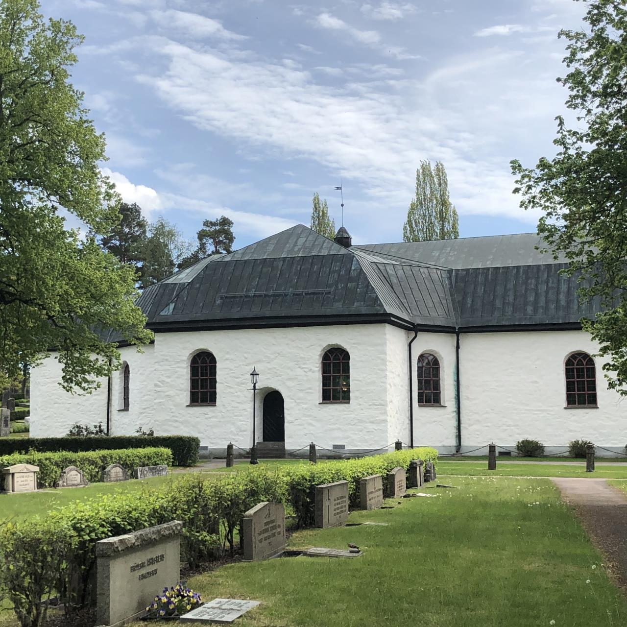 Nedre Ulleruds vita kyrka i solljus med en något molnig himmel