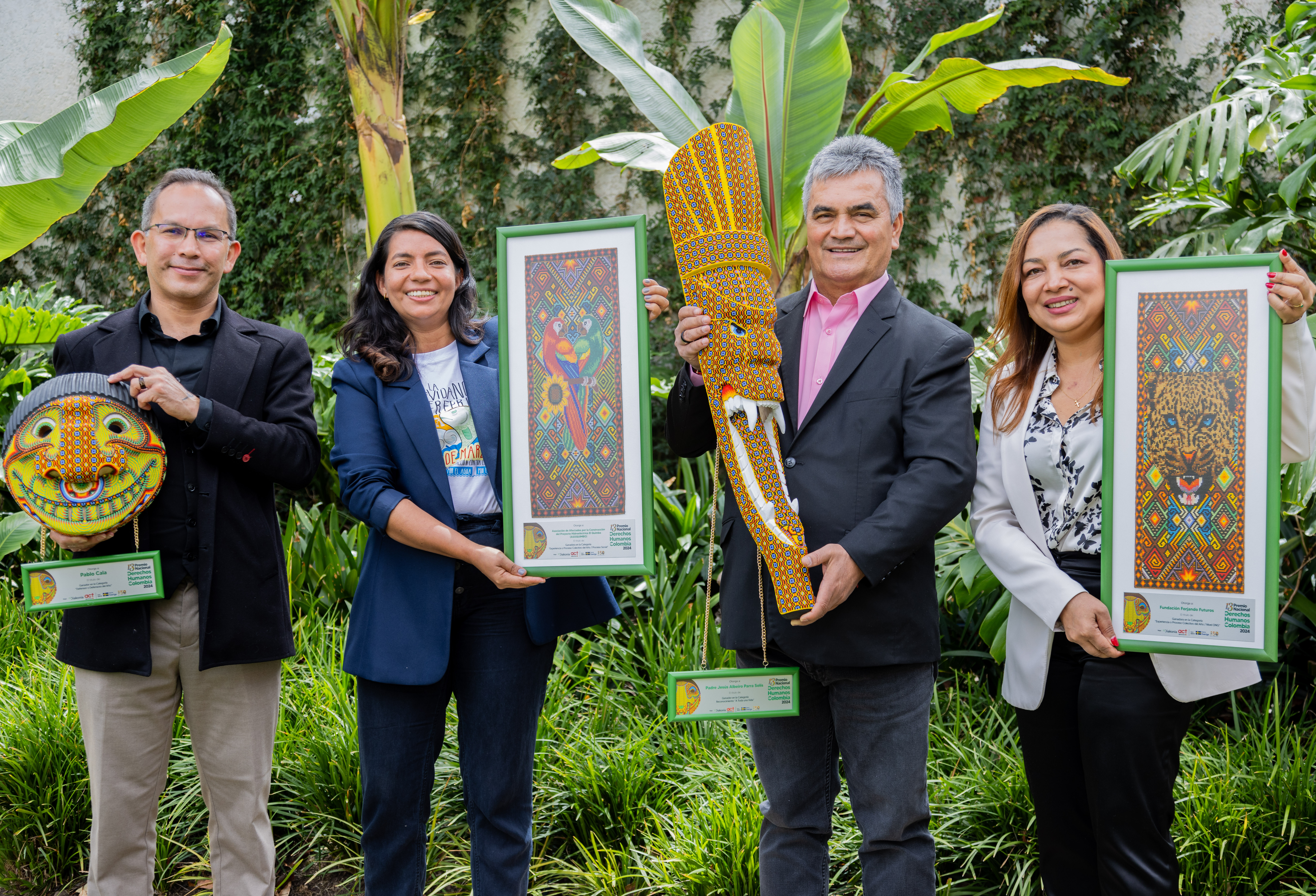 Två män och två kvinnor från Colombia håller upp konstverk framför djungelväxtlighet.