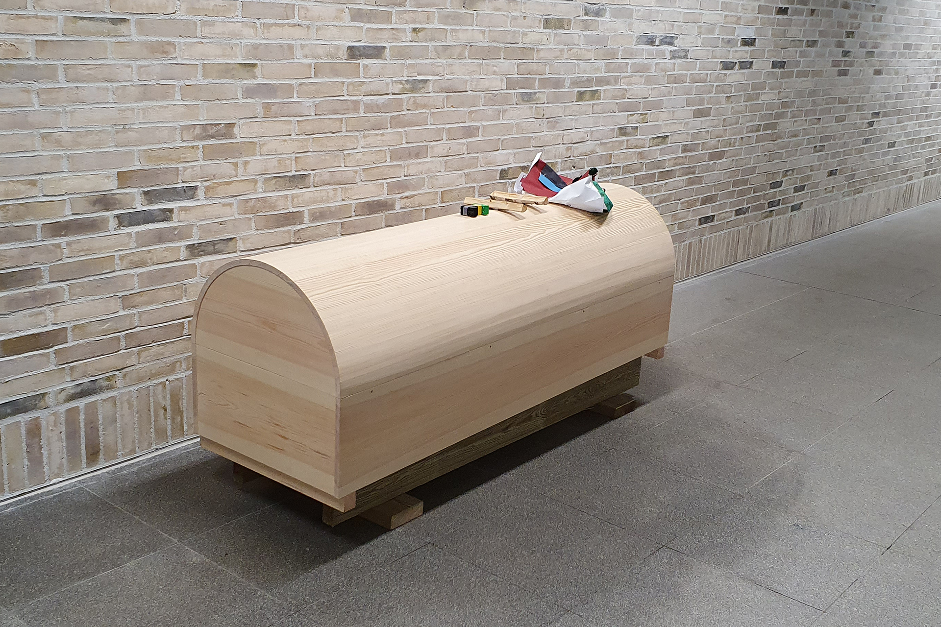 Ljus träkista med välvt lock framför ljus tegelvägg.