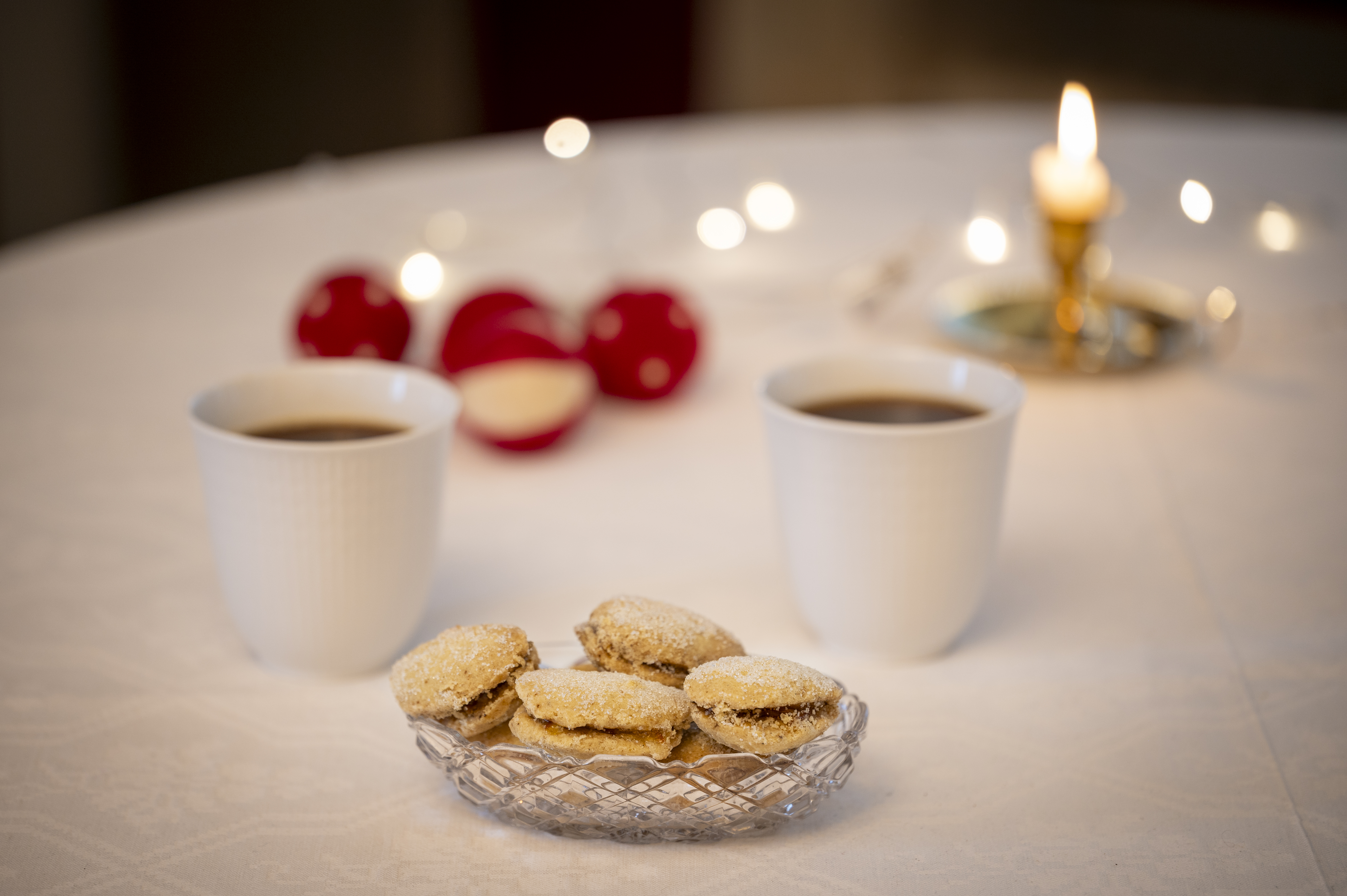 Småkakor, kaffe och ljus på bord med vit duk