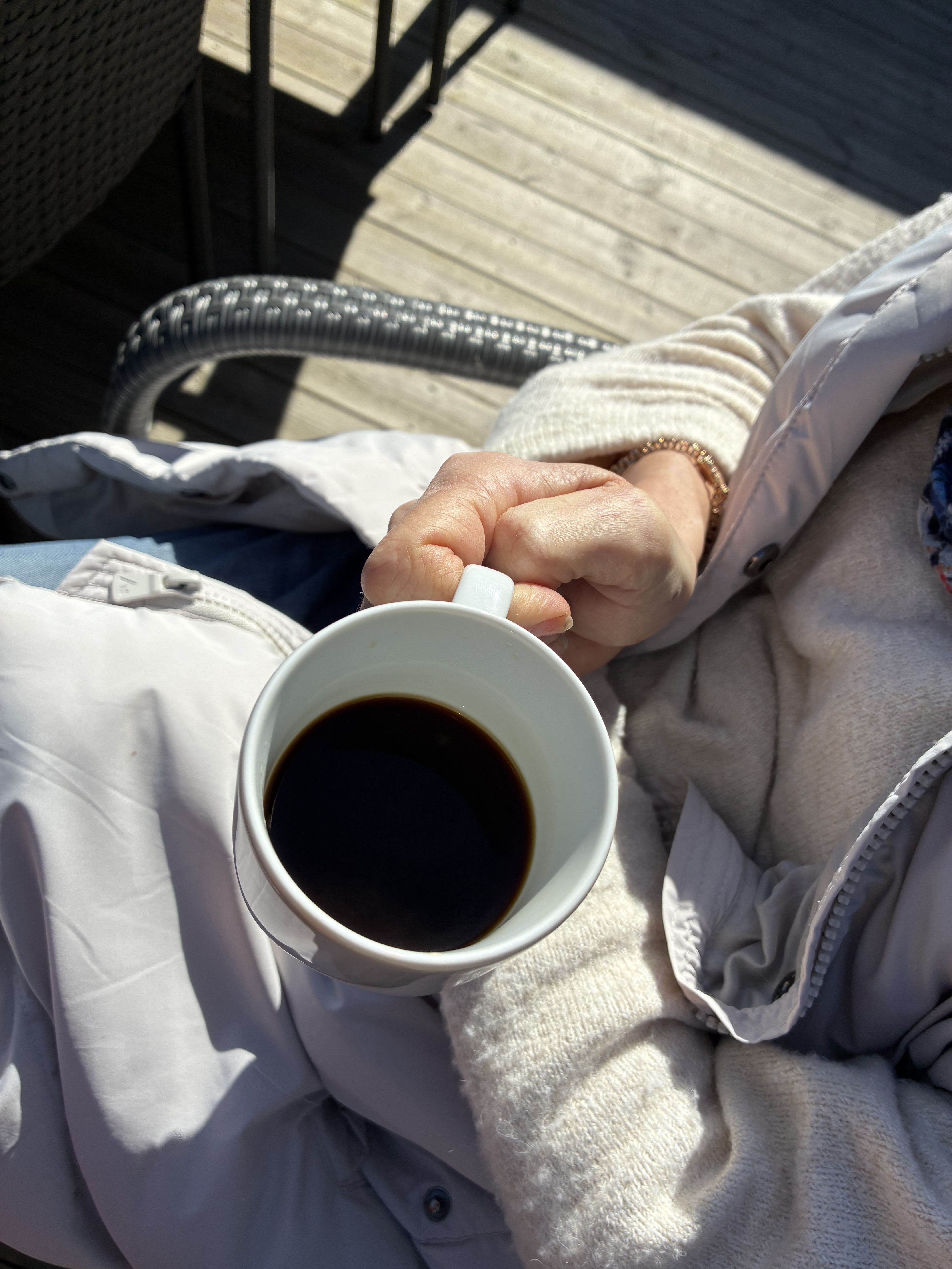 ett par händer som håller en kaffeopp och ett trädäck nedanför