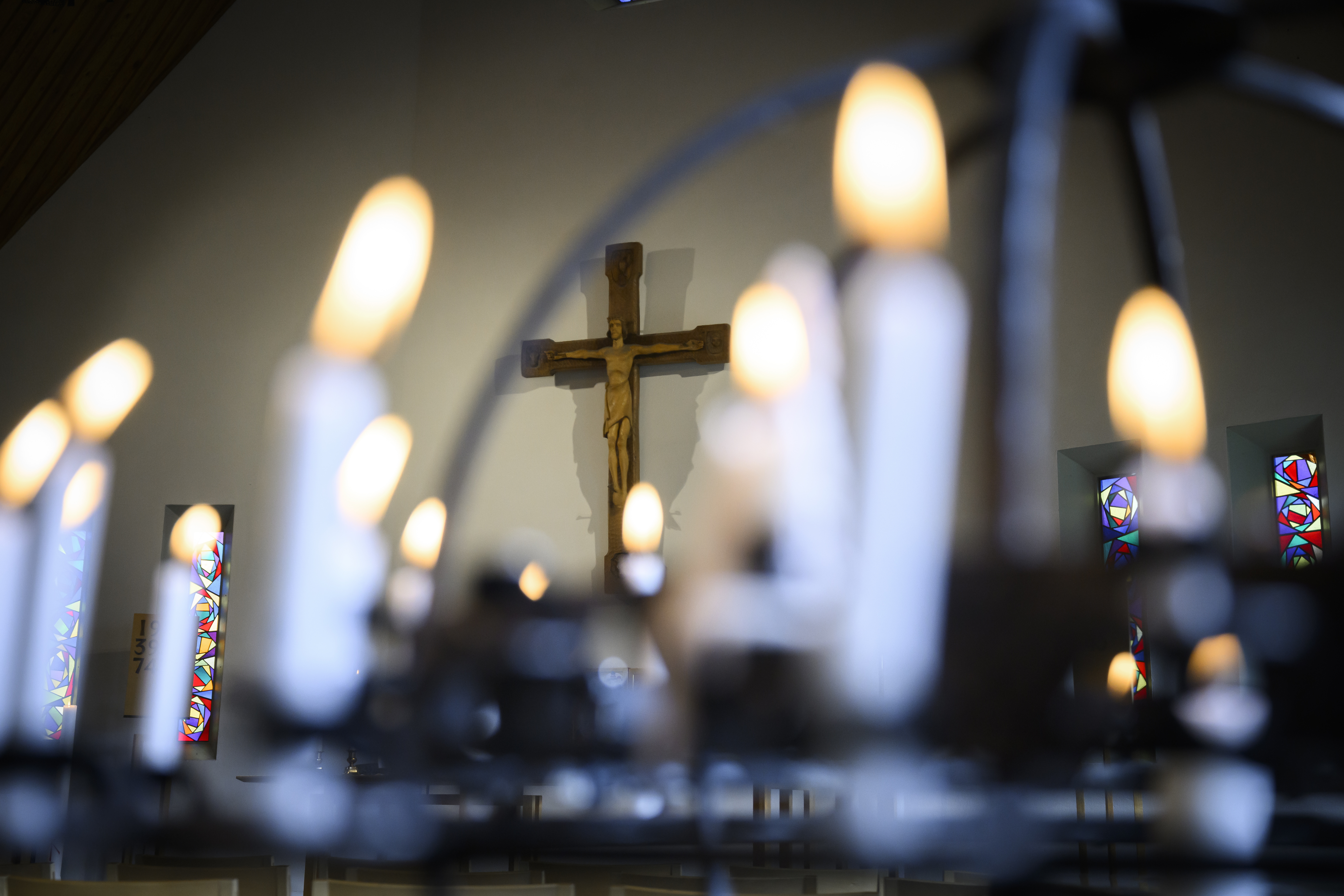 Tända stearinljus med kors i bakgrunden i en kyrka.