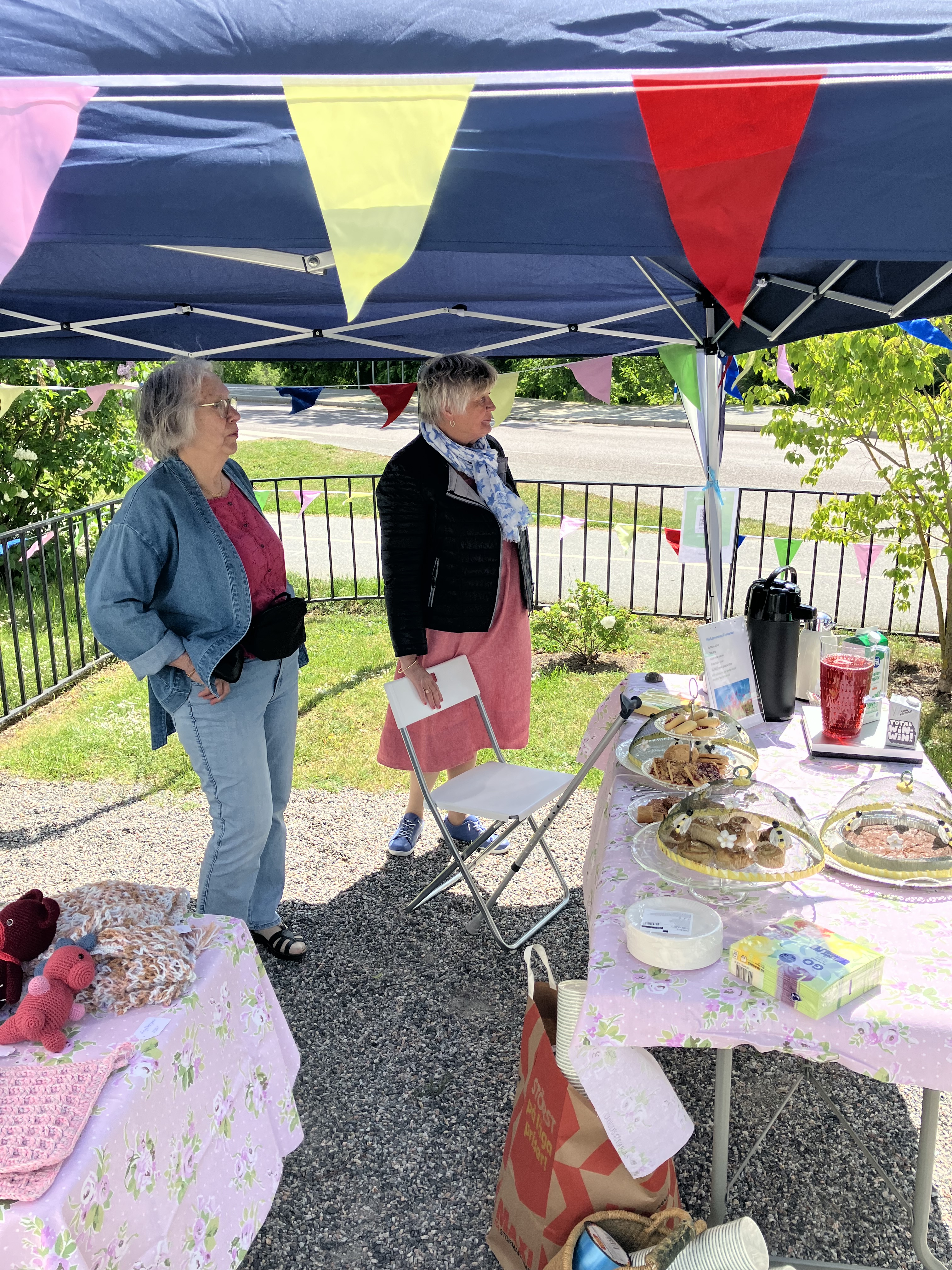 Två kvinnor står och bjuder på fika under ett partytält.