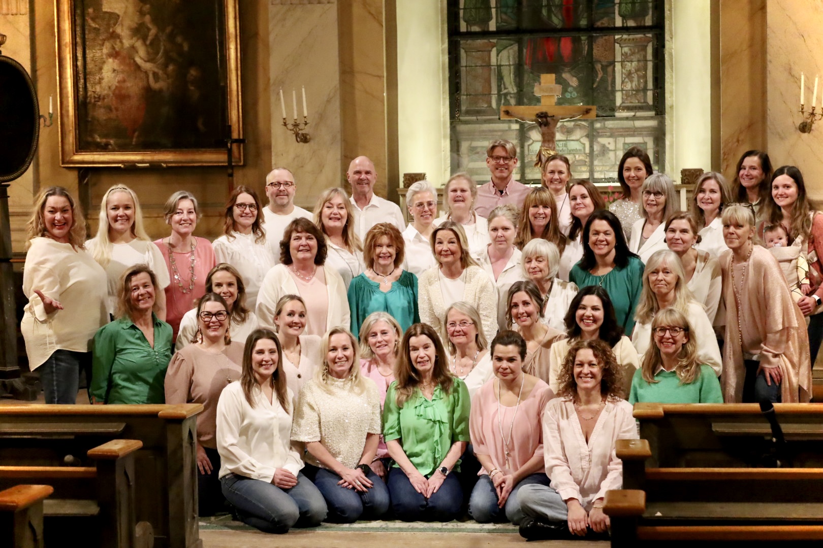 Kör står med framför ett altare. Alla har ljusa kläder i rosa och aprikost, några gröna tröjor.