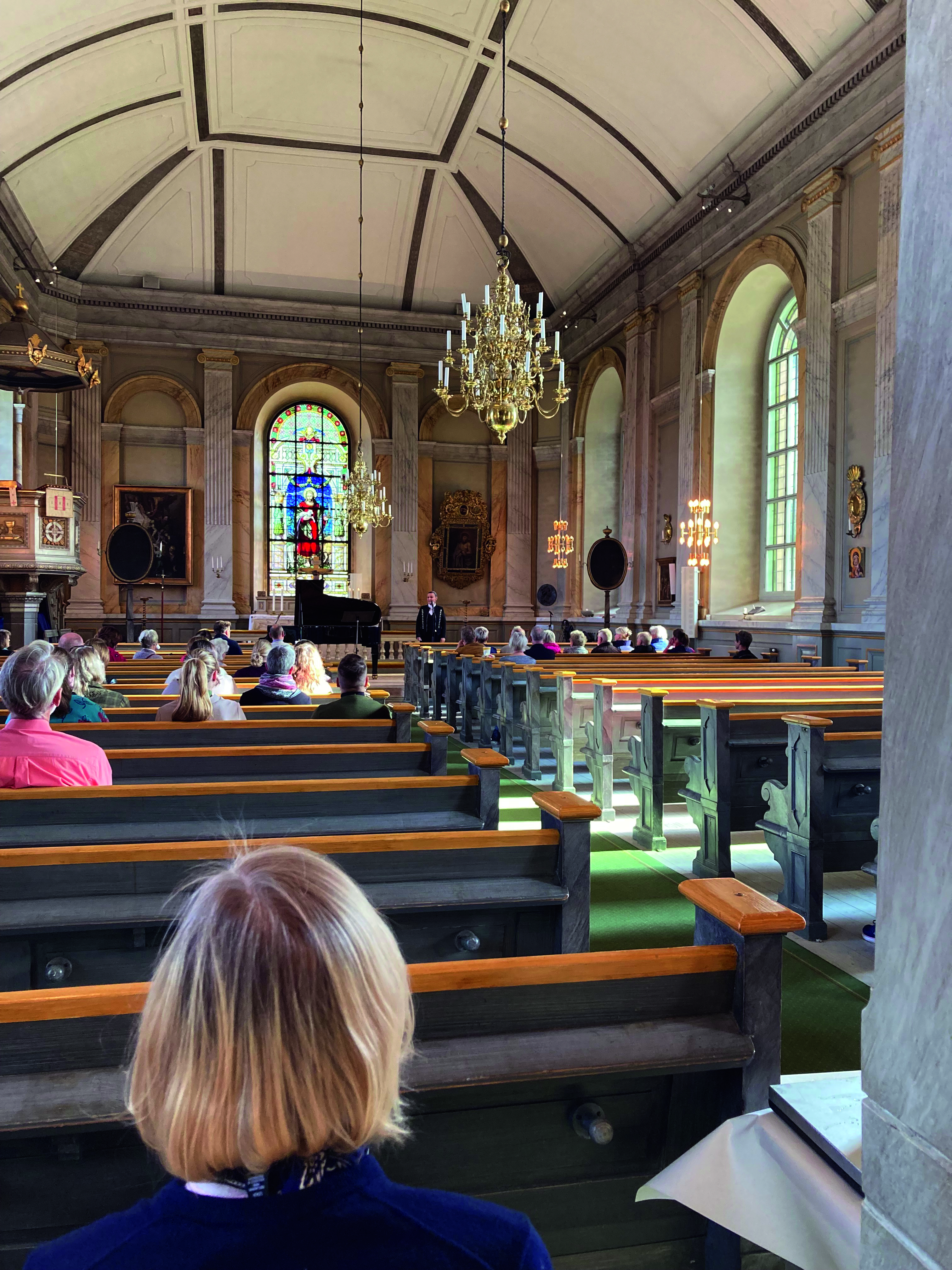 Inifrån Vaxholms kyrka. Människor sitter utspridda.
