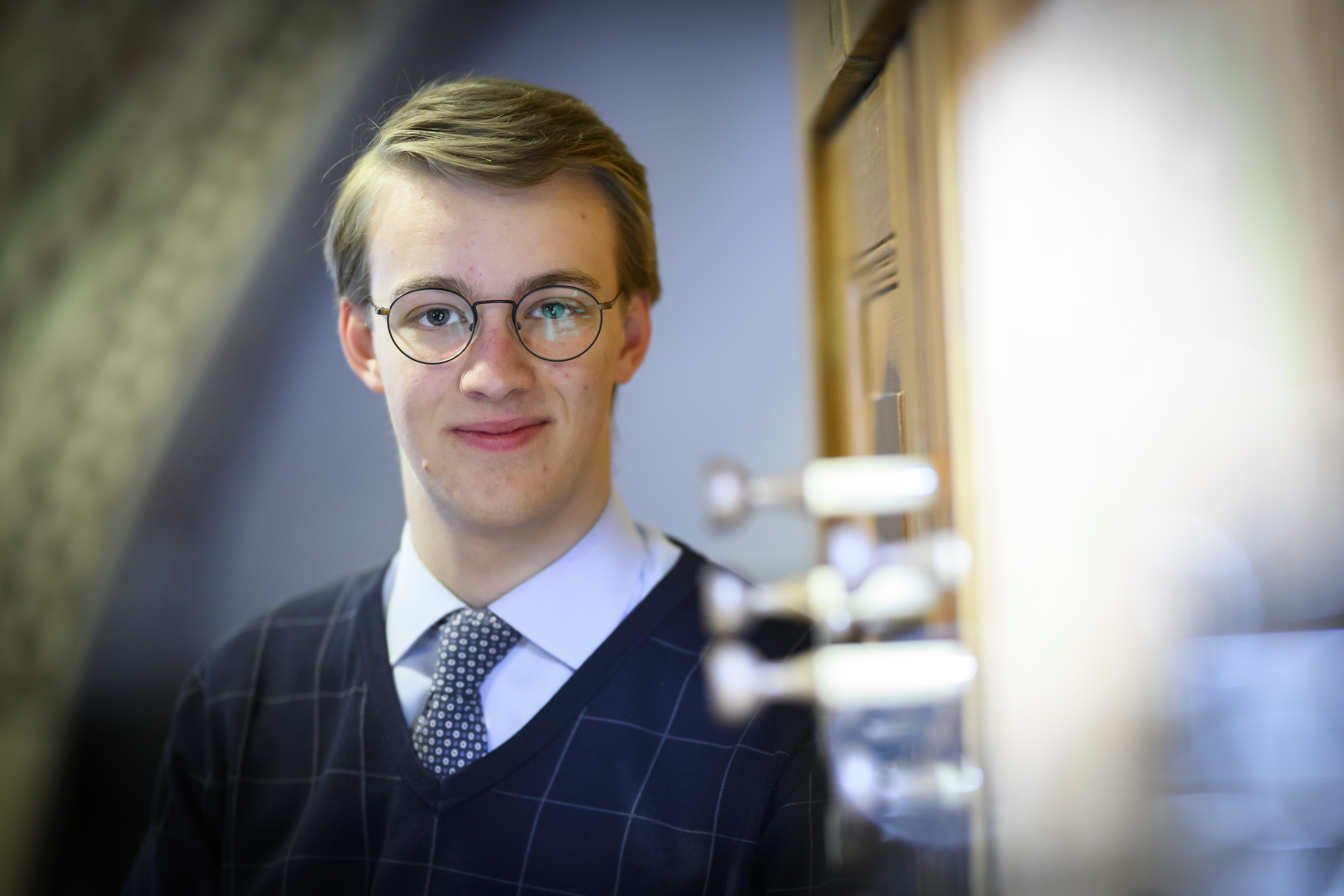 En kille i övre tonåren sitter vid en kyrkorgel. Han är klädd i skjorta och slips och ler mot kameran.