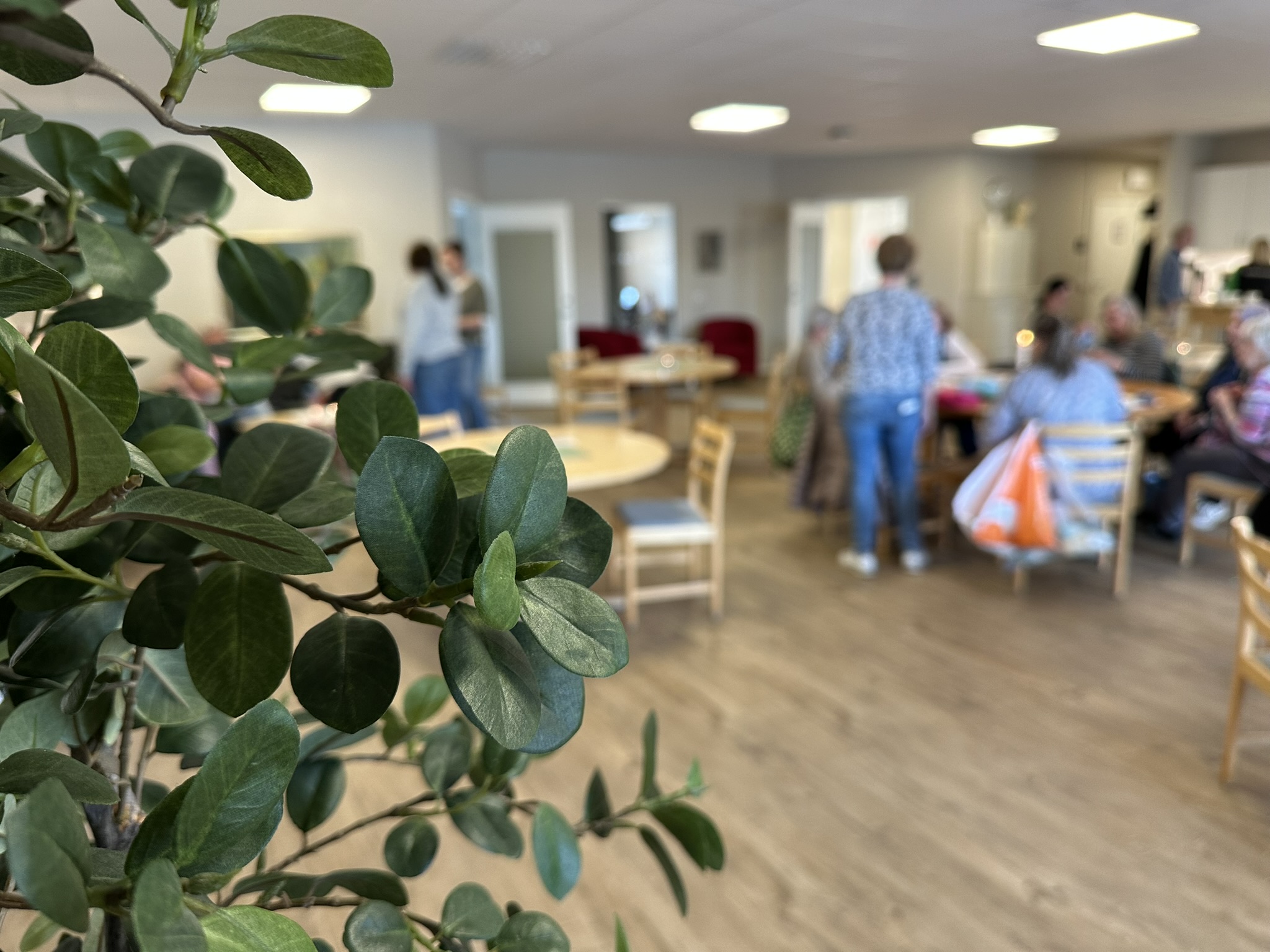 Människor i olika åldrar sitter och fikar vid flera runda bord.